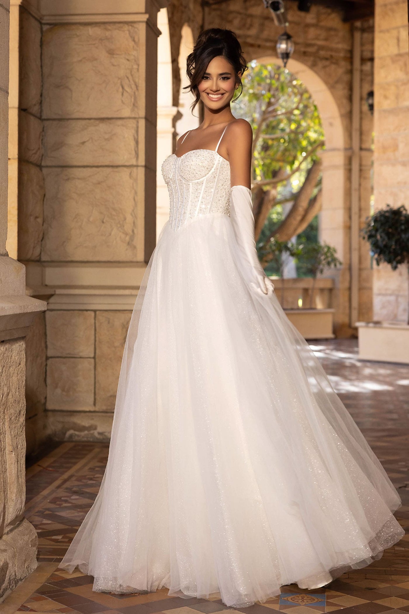 Woman in a white wedding dress standing in an outdoor setting with stone architecture.