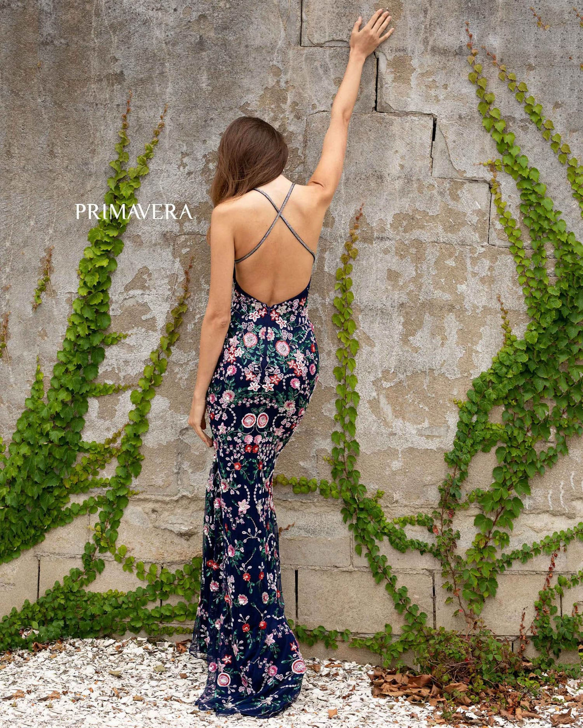 Woman in a floral dress against a stone wall with greenery