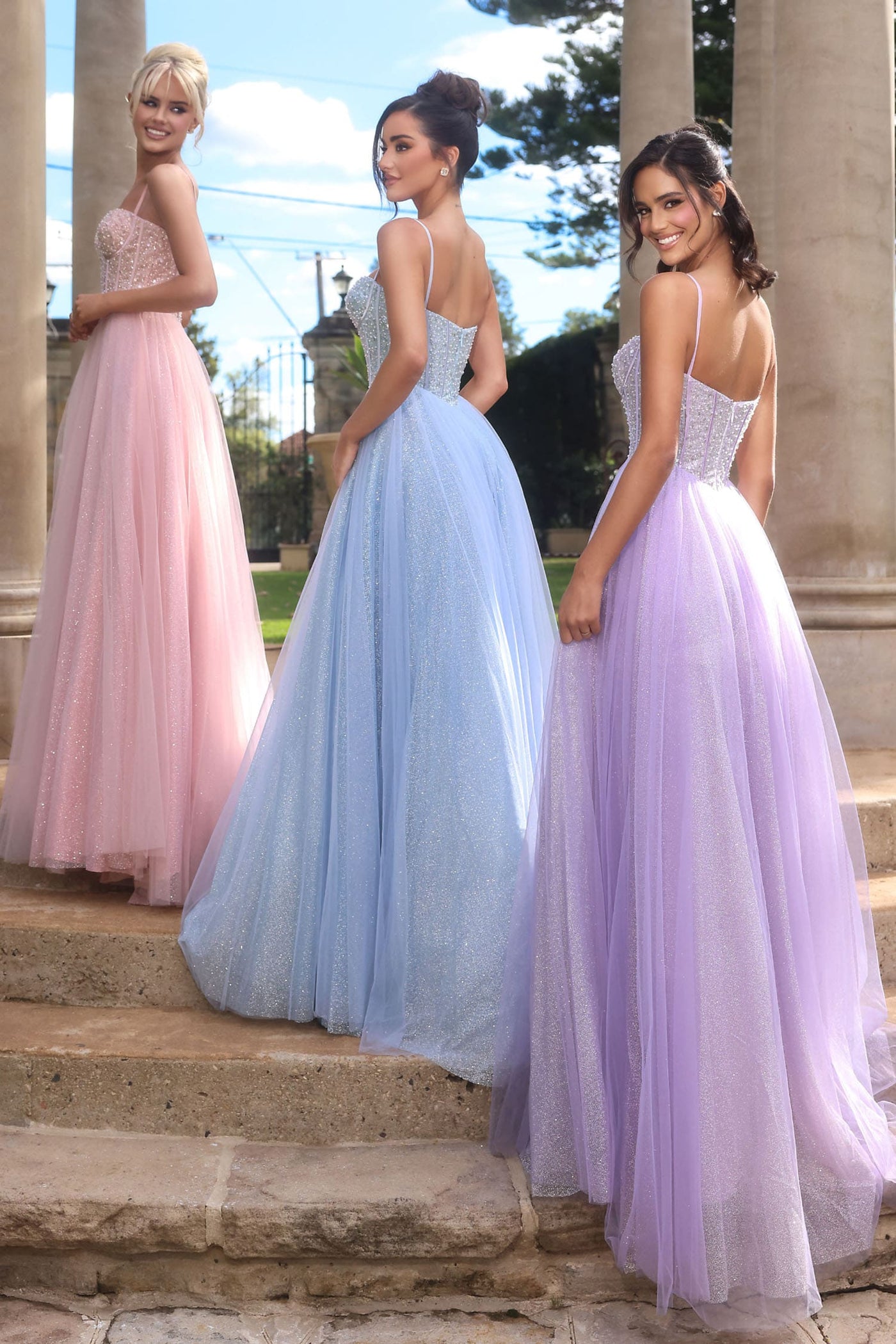 Three women in long, elegant dresses standing on steps outdoors.