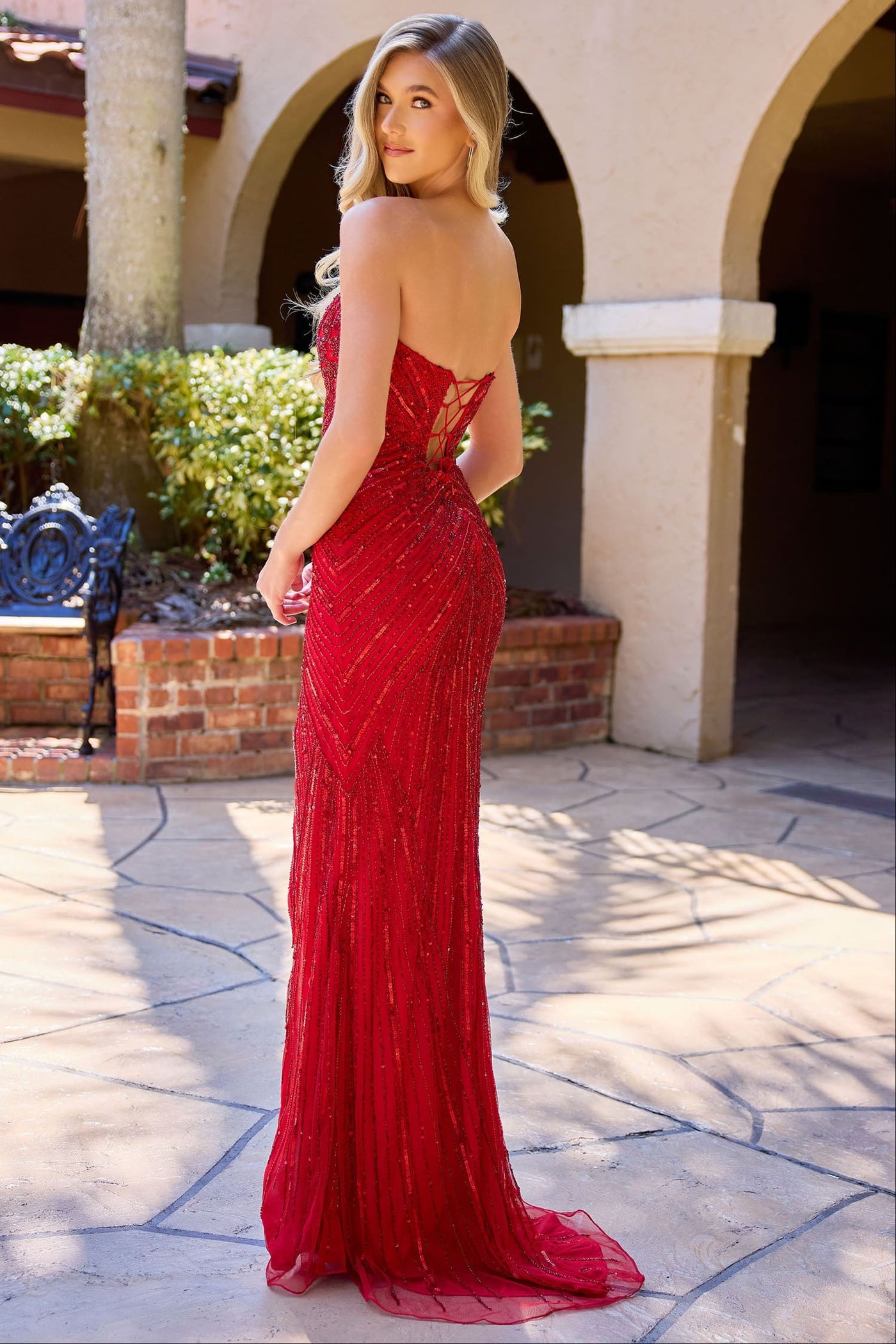 Woman in a red evening gown standing outdoors on a stone patio.