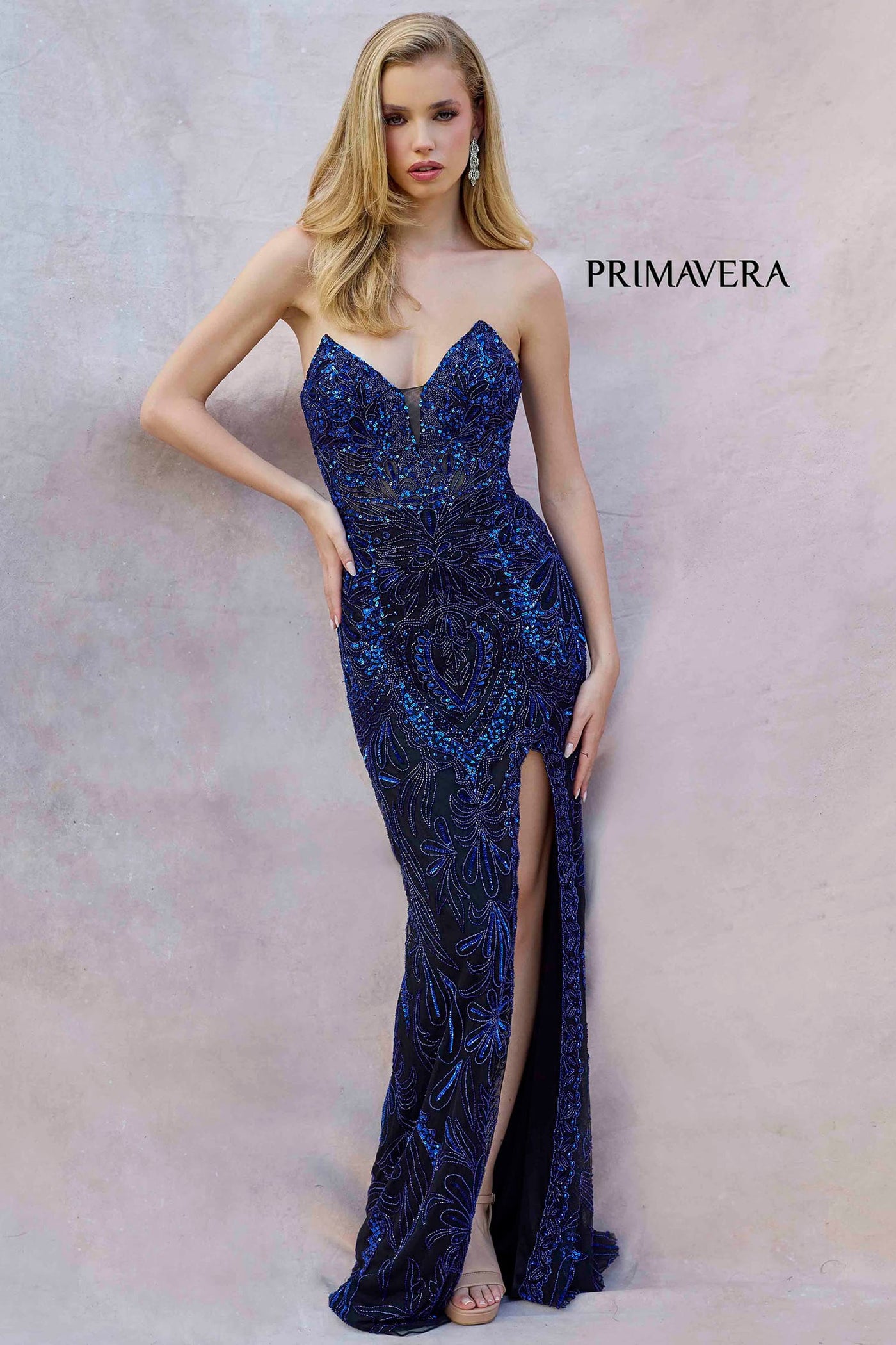 Woman wearing a blue sequin evening gown with a slit on a plain background, branded 'Primavera'.