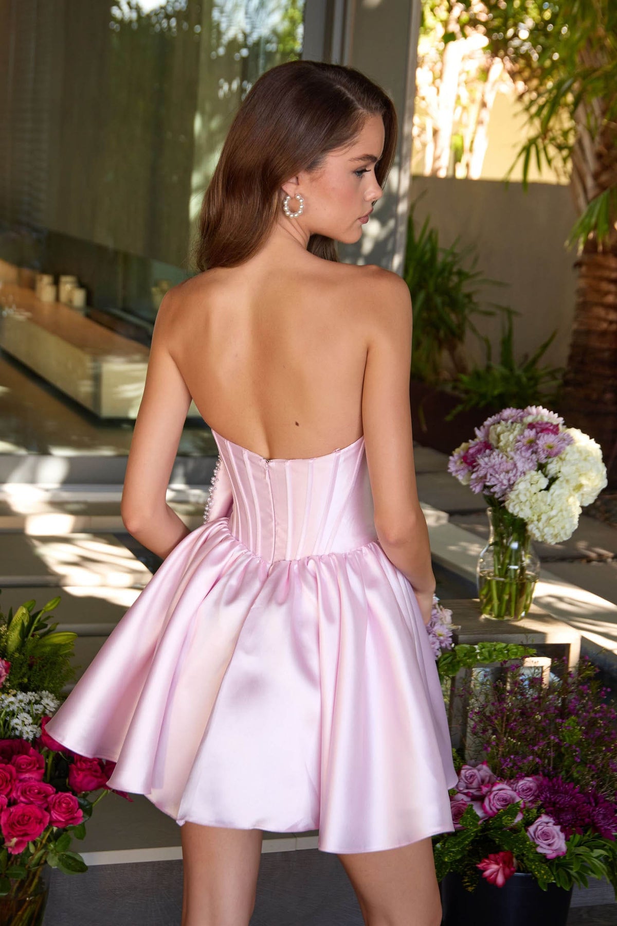 Woman in a pink dress standing outdoors with flowers and plants around.