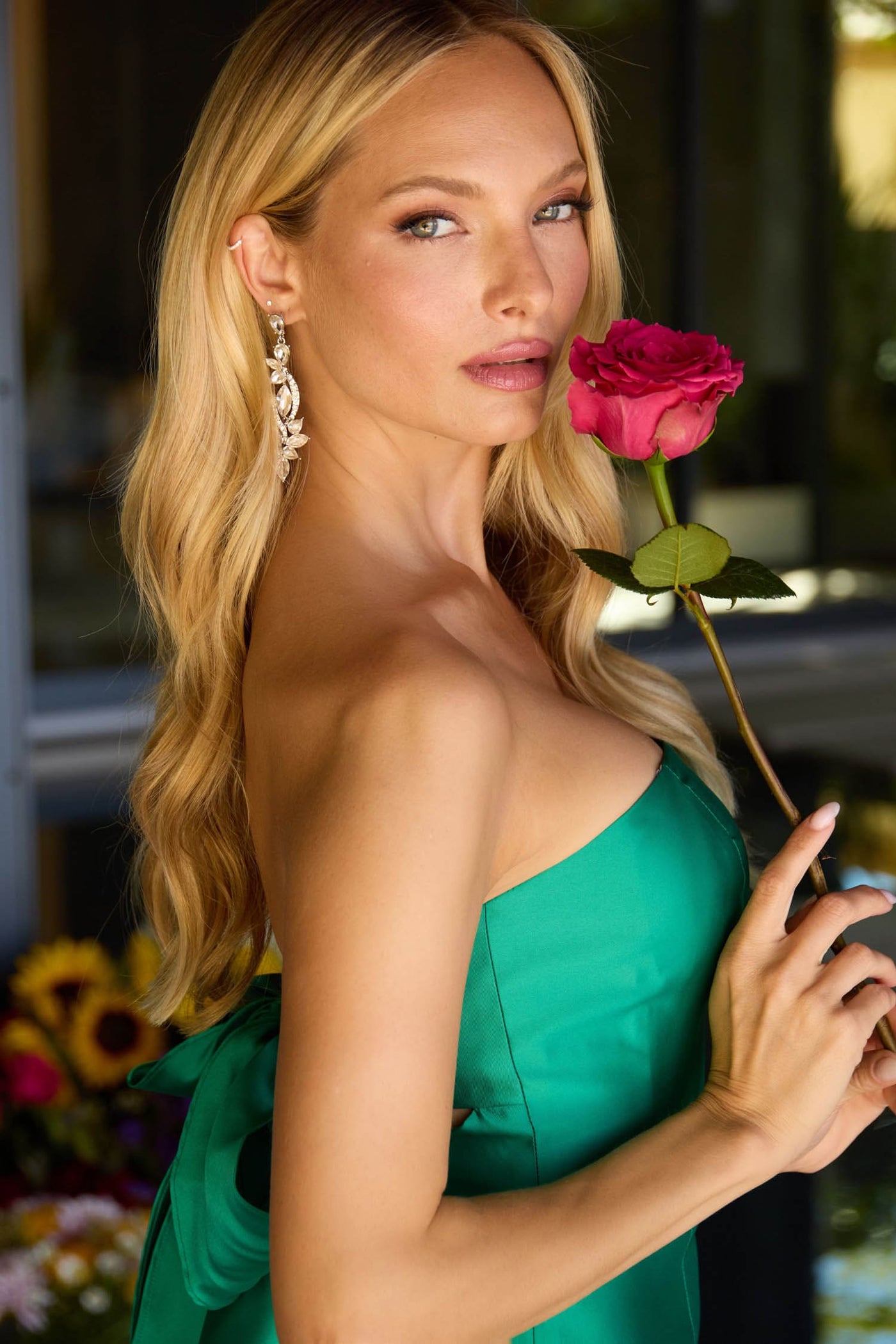 Woman in a green dress holding a pink rose with a blurred background