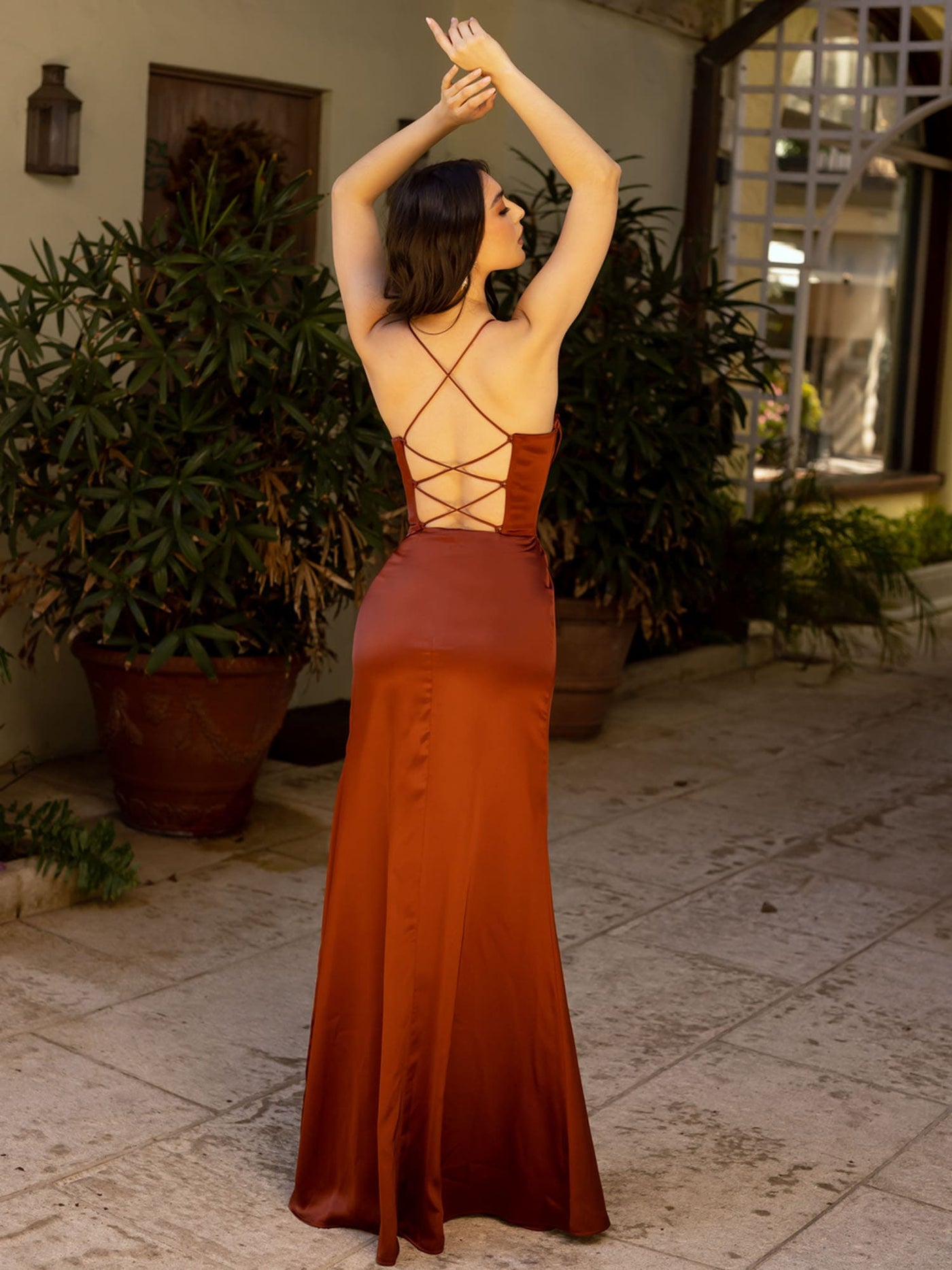 Woman in a rust-colored dress with criss-cross back design standing in an outdoor setting.