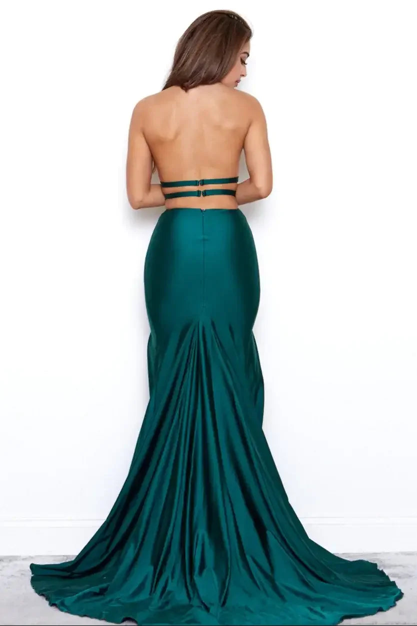 A woman wears a form-fitting, backless, emerald green gown with a long train, standing with her back to the viewer against a plain white background.