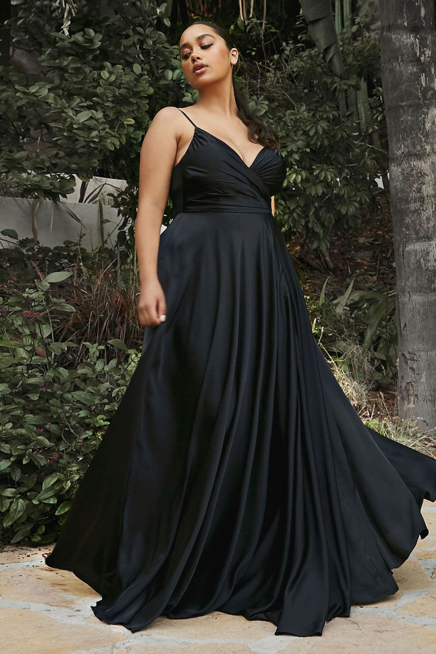 Woman in a black evening gown standing outdoors with greenery in the background