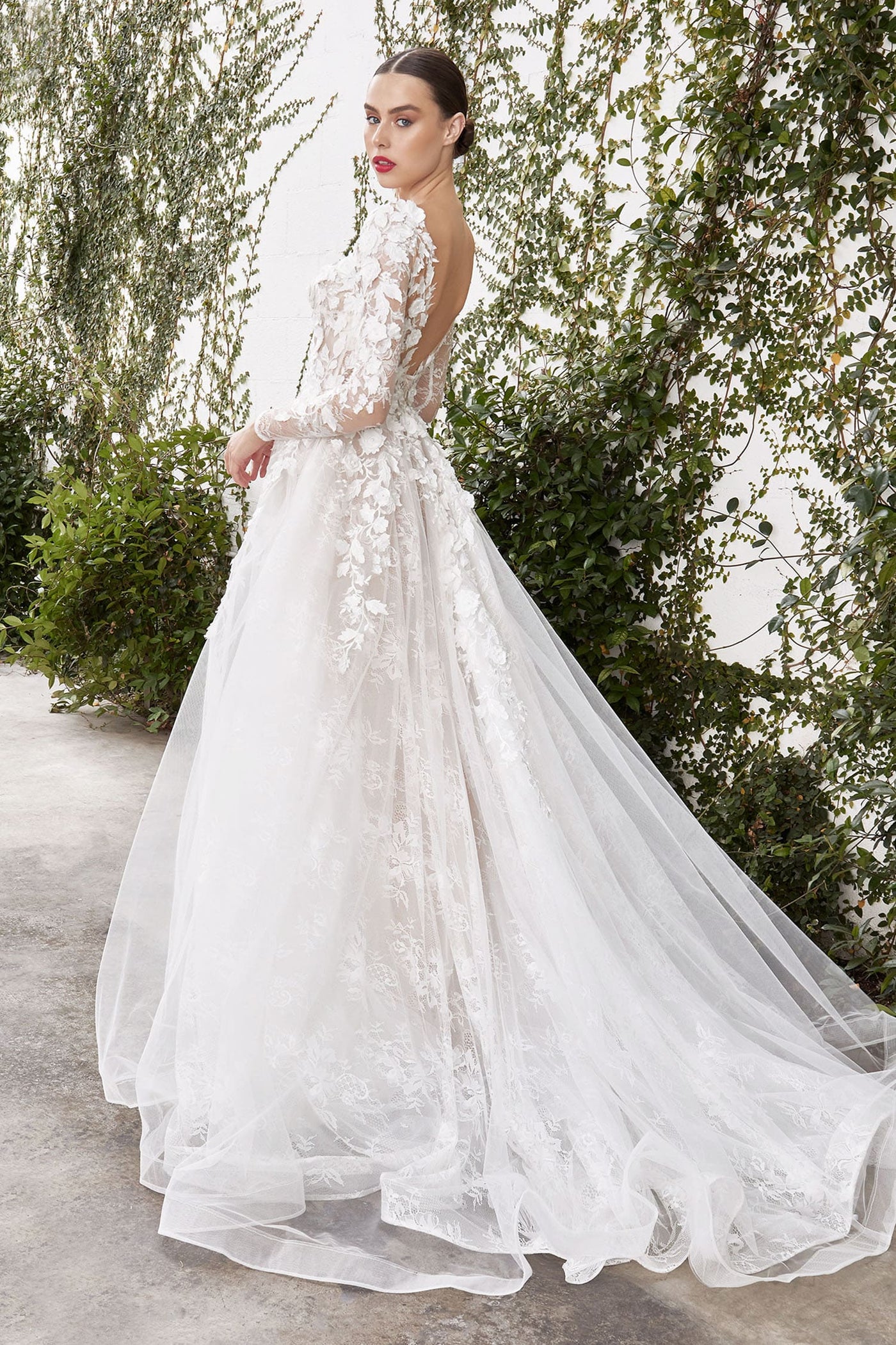 Woman in a white floral wedding dress standing outdoors with greenery in the background