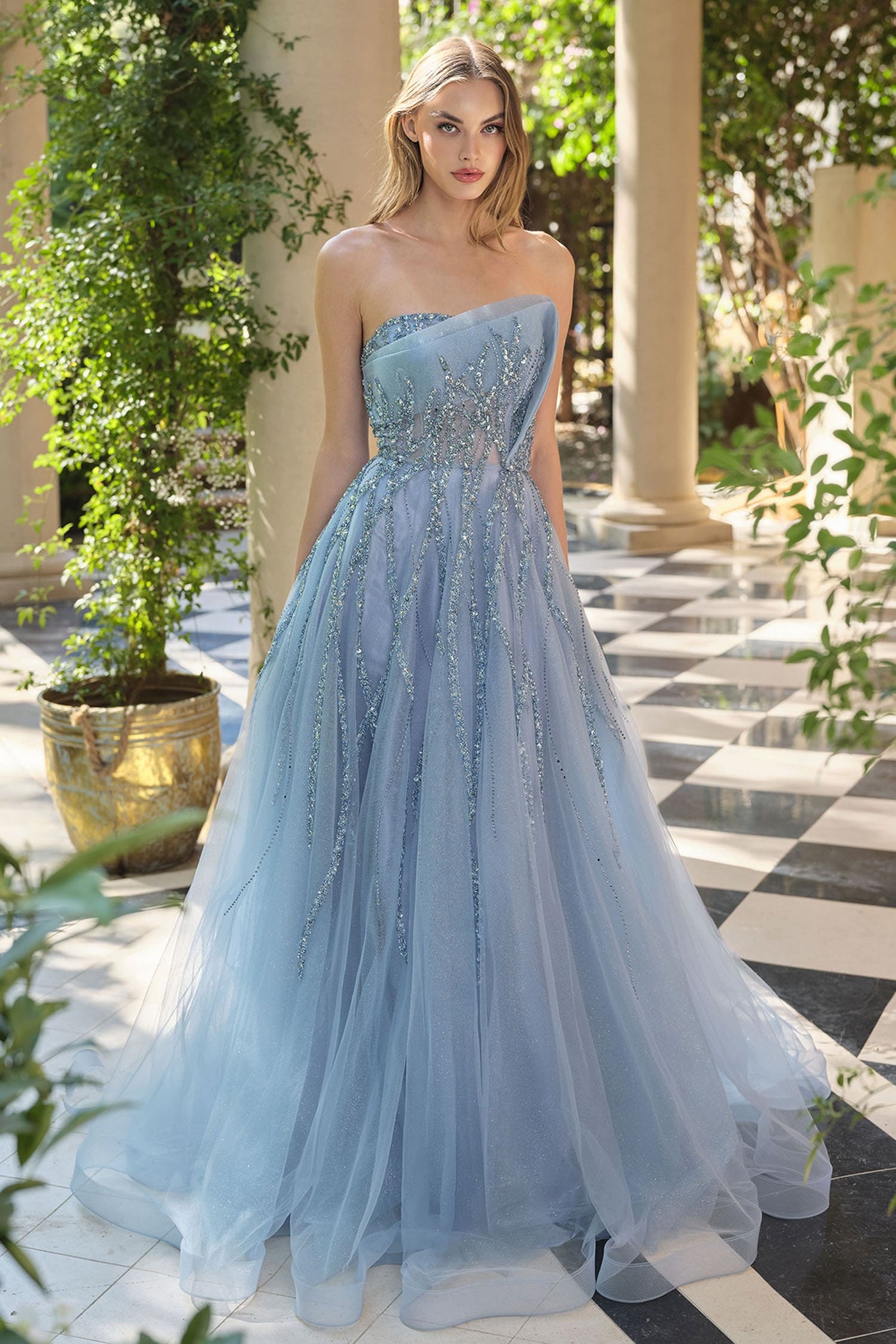 Woman in a light blue strapless gown with beaded details standing in an outdoor setting.