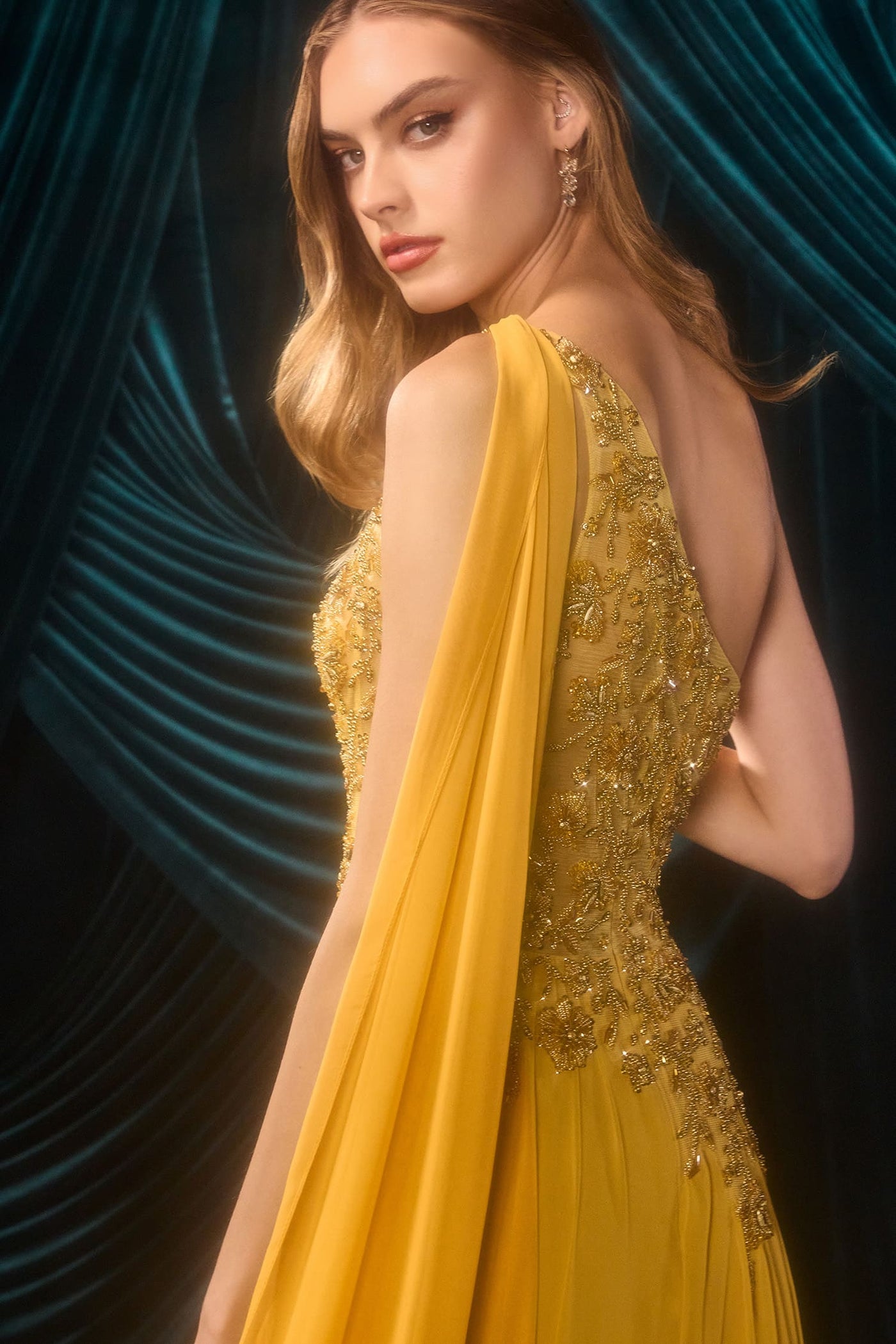Woman wearing a yellow evening gown with a dark blue curtain background