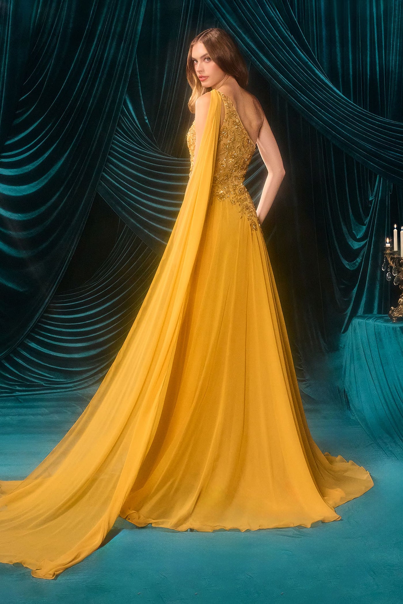Woman in a yellow evening gown with intricate detailing against a blue curtain backdrop