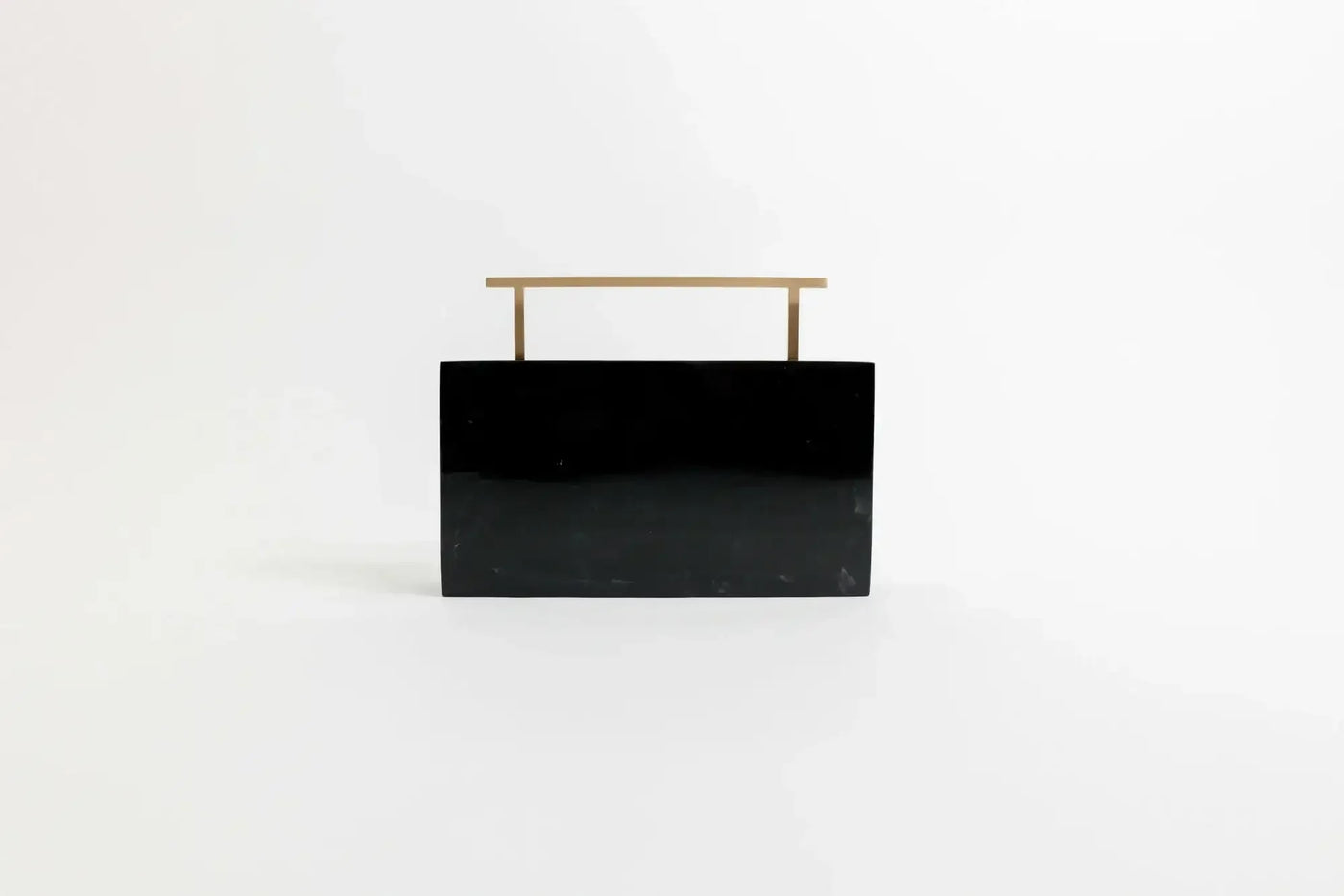 A black rectangular object with a sleek brass handle on top, standing upright against a plain white background.