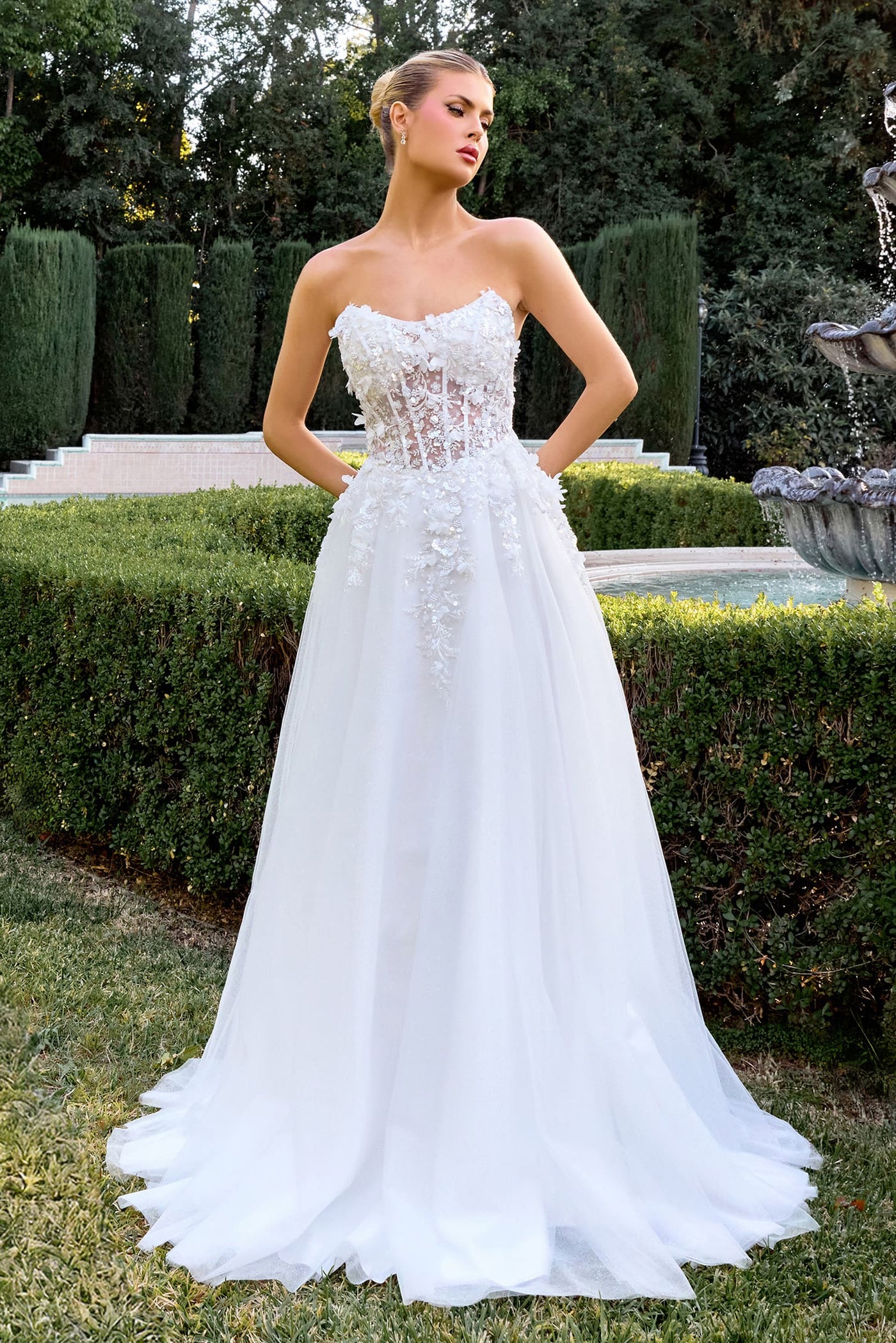Woman wearing a white strapless wedding dress in an outdoor setting with greenery.
