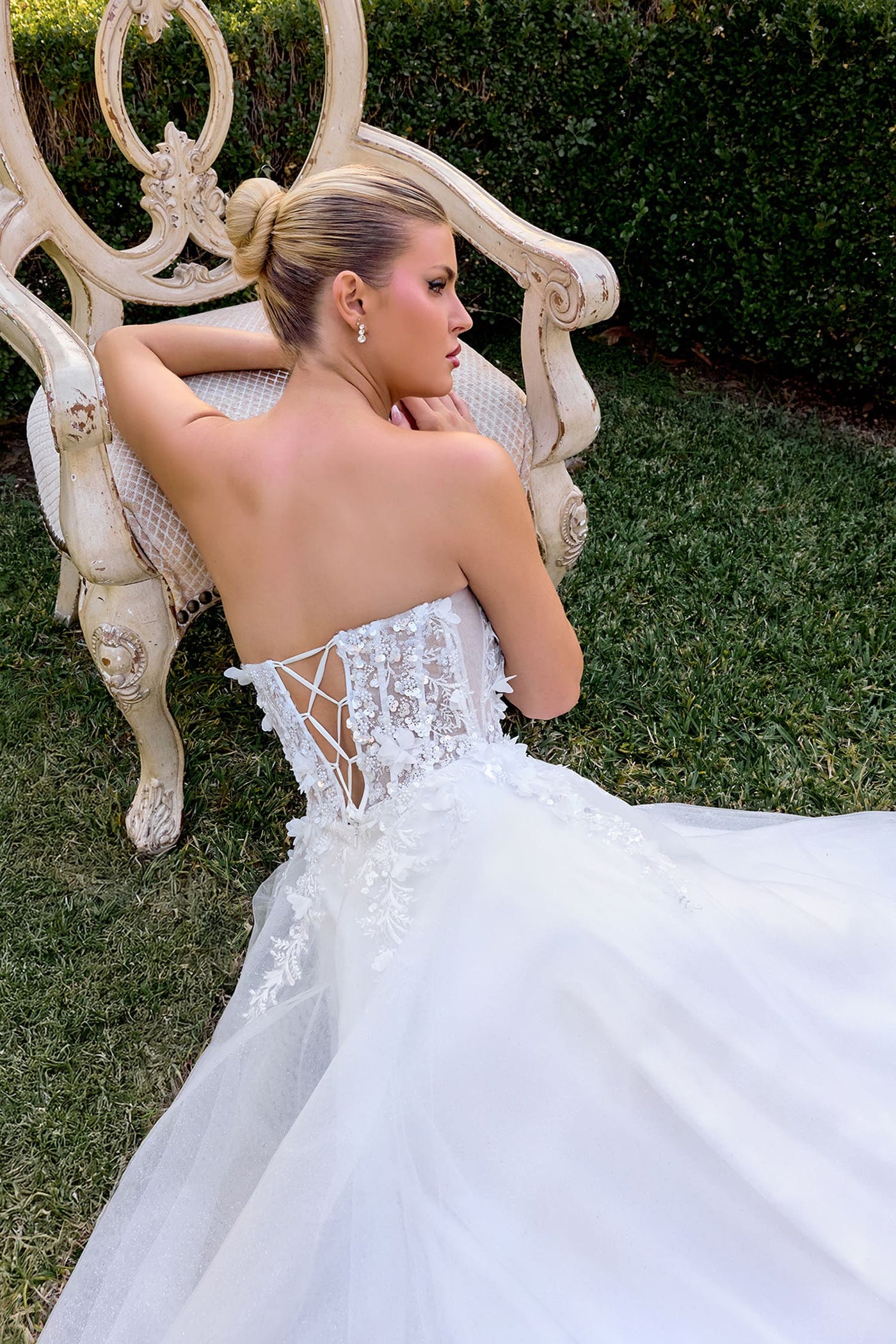 Woman in a white wedding dress sitting on an ornate chair outdoors.