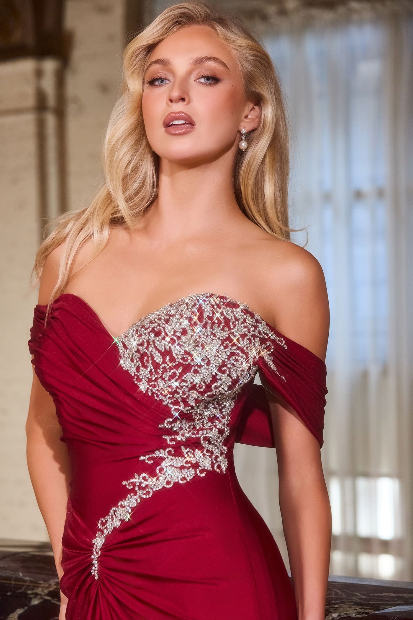 Woman wearing a red off-shoulder dress with lace details in an indoor setting.
