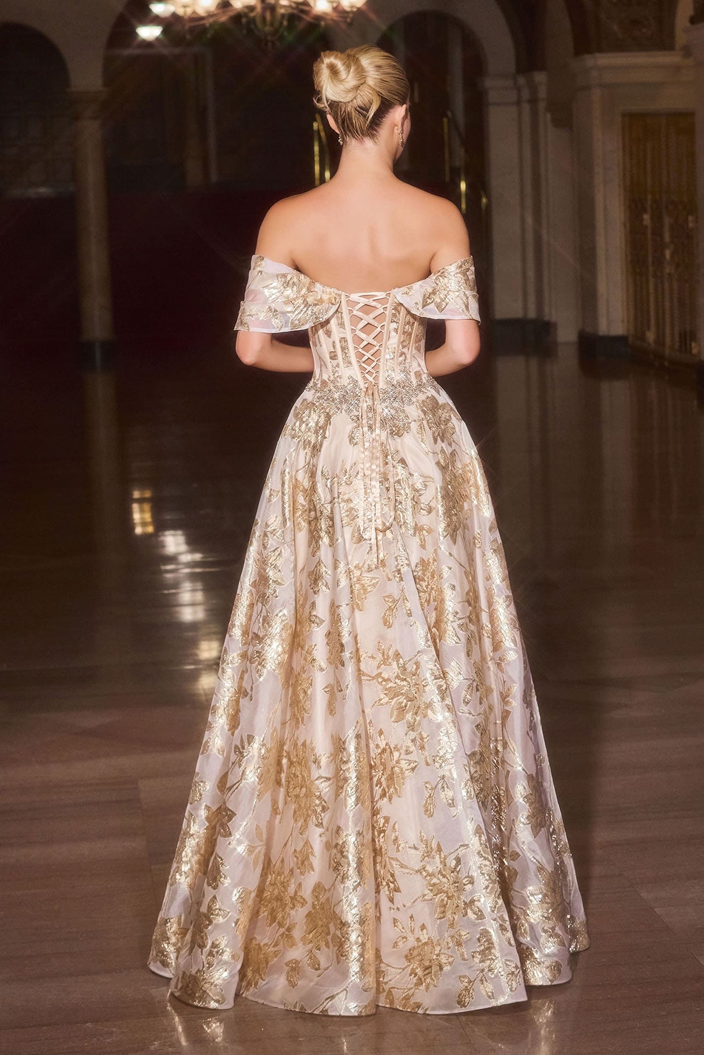 Woman in a gold evening gown with intricate detailing in an elegant indoor setting.