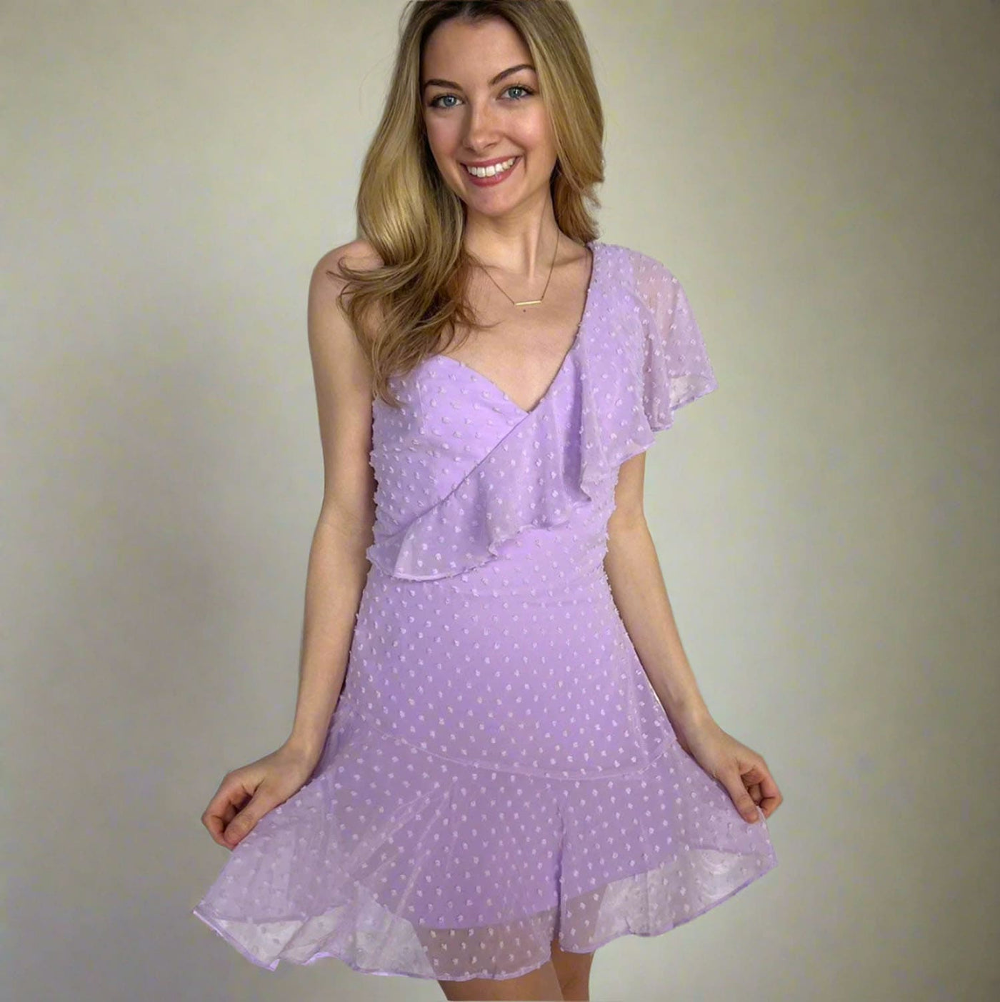 A woman modeling a light purple sleeveless dress with white polka dots, featuring a ruffled wrap-style bodice and flutter sleeves, set against a plain beige studio background.