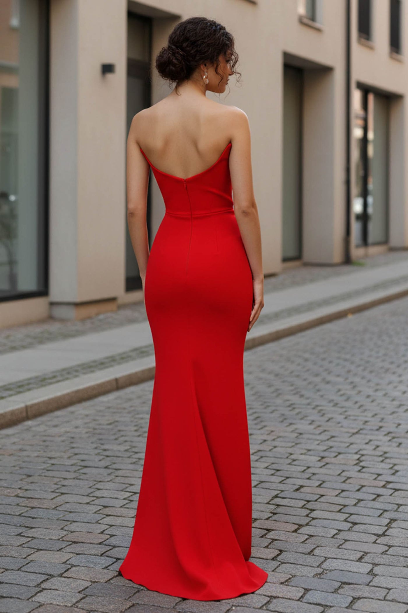 Woman in a red dress standing on a street with buildings in the background