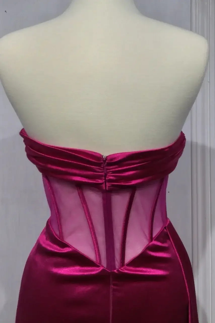 A magenta strapless dress is displayed on a mannequin, featuring a structured mesh bodice and a fitted silhouette. The backdrop is a plain, light-colored wall.