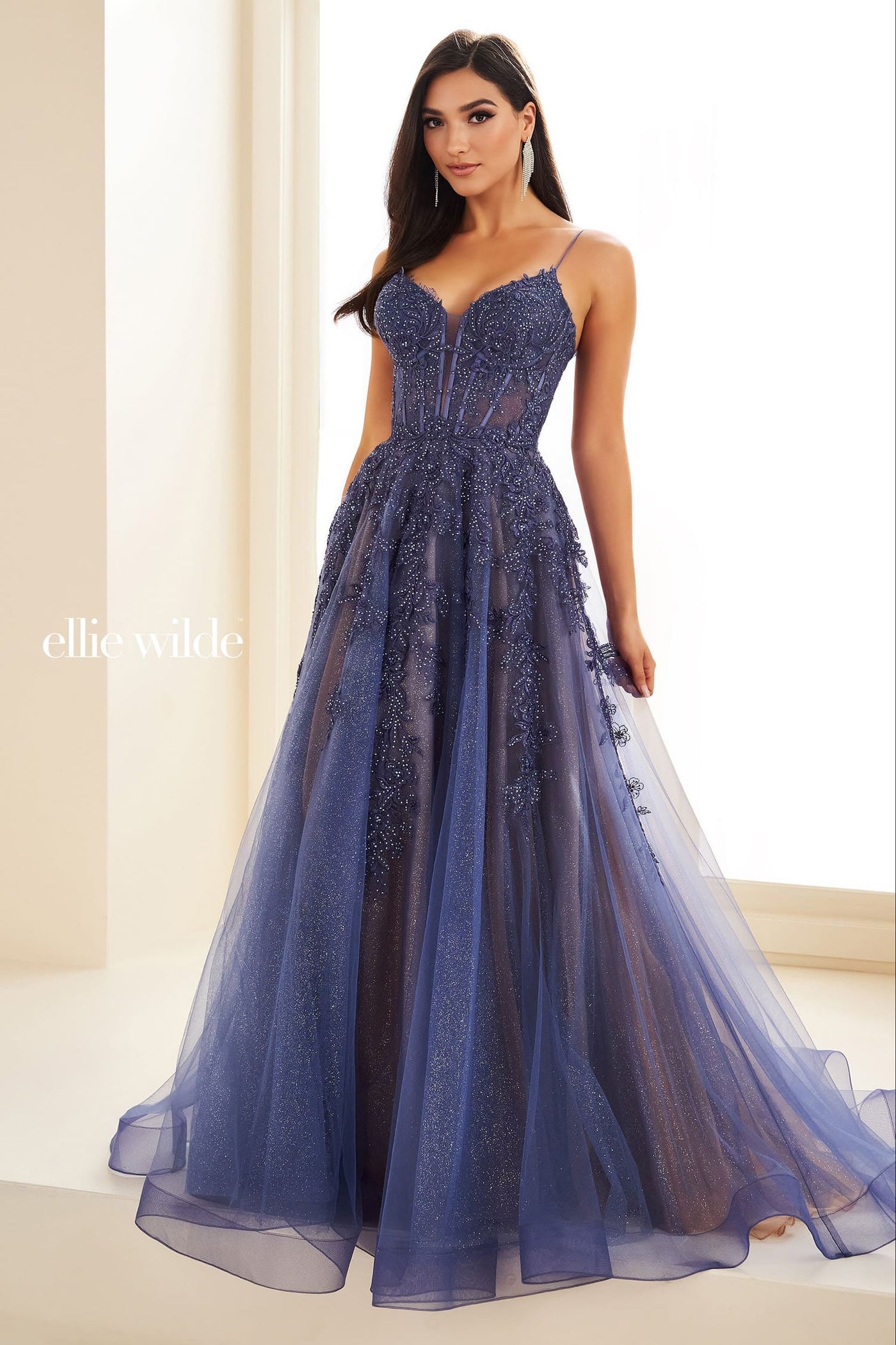 Woman wearing a blue evening gown with intricate detailing, standing against a neutral background.