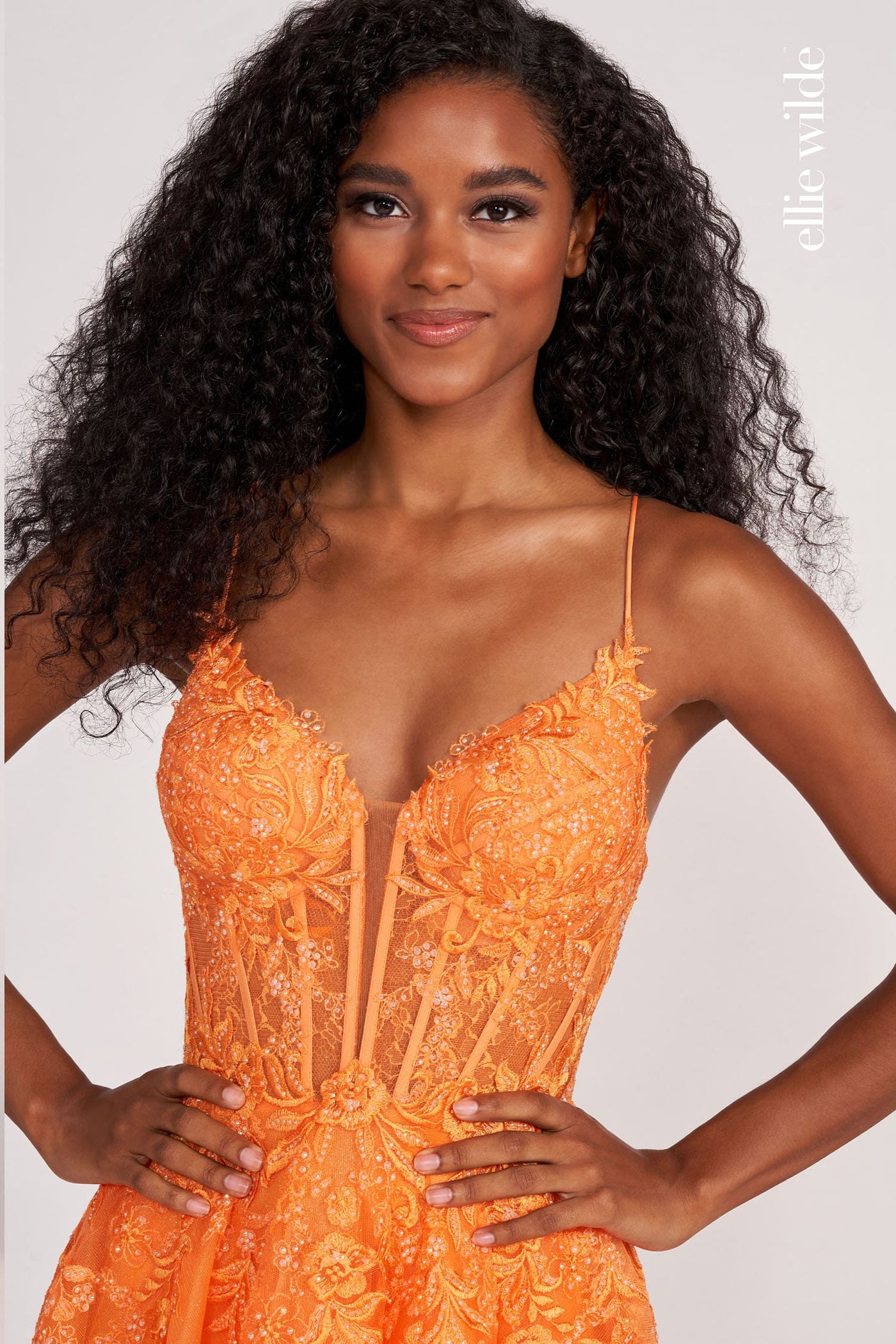 Woman wearing an orange lace dress against a plain background