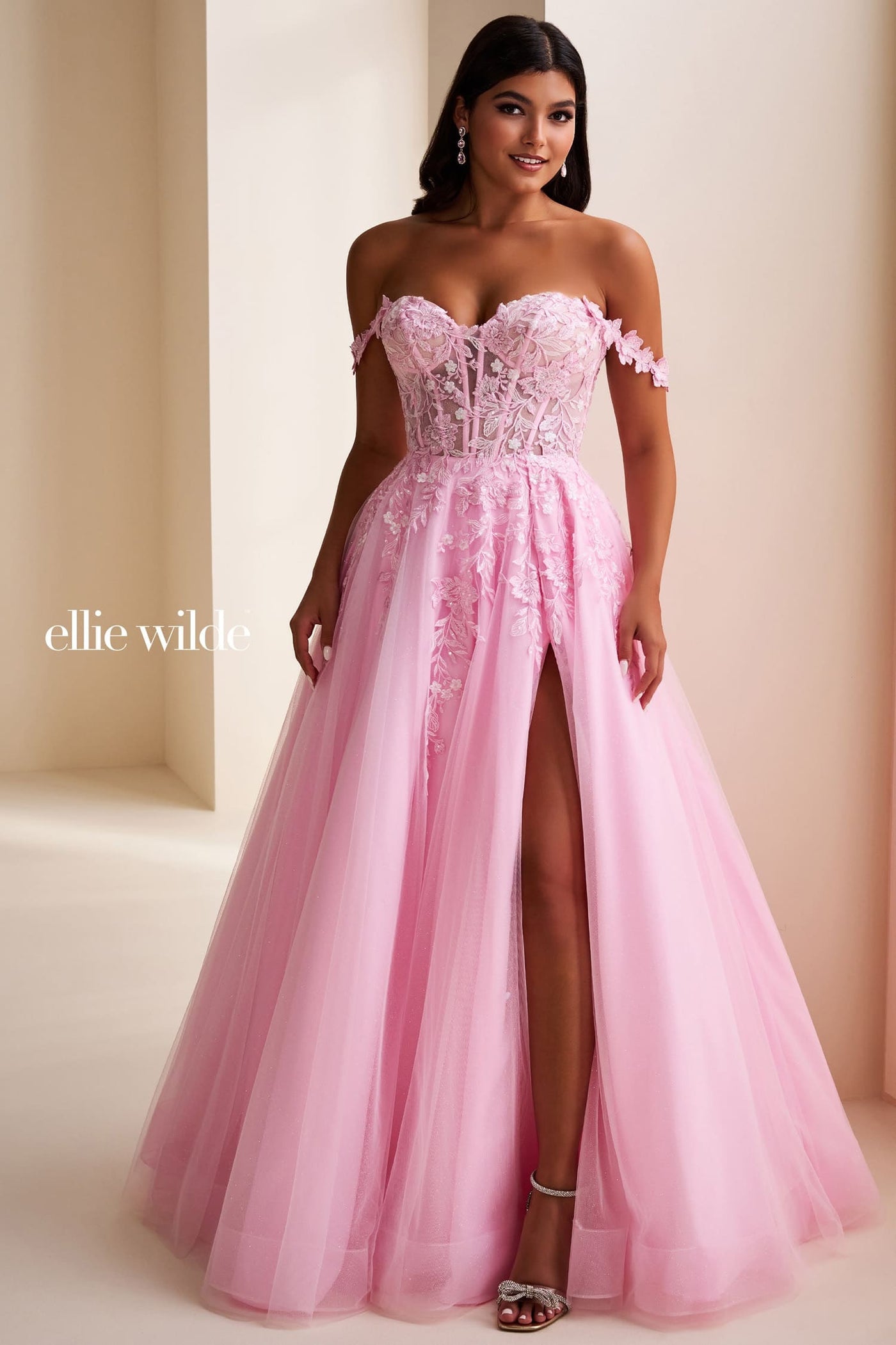 Woman wearing a pink evening gown with a high slit, standing against a plain background.