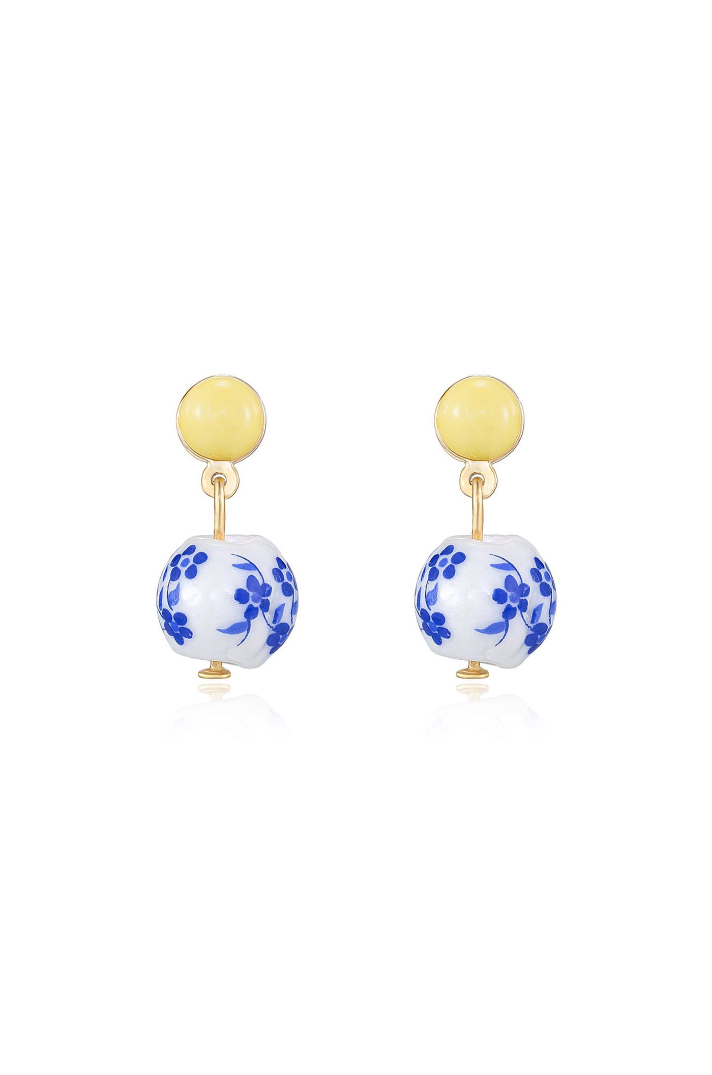 Gold-tone earrings feature a yellow circular top with a blue floral-patterned porcelain ball dangling below. They appear on a reflective surface, highlighting their design and materials.