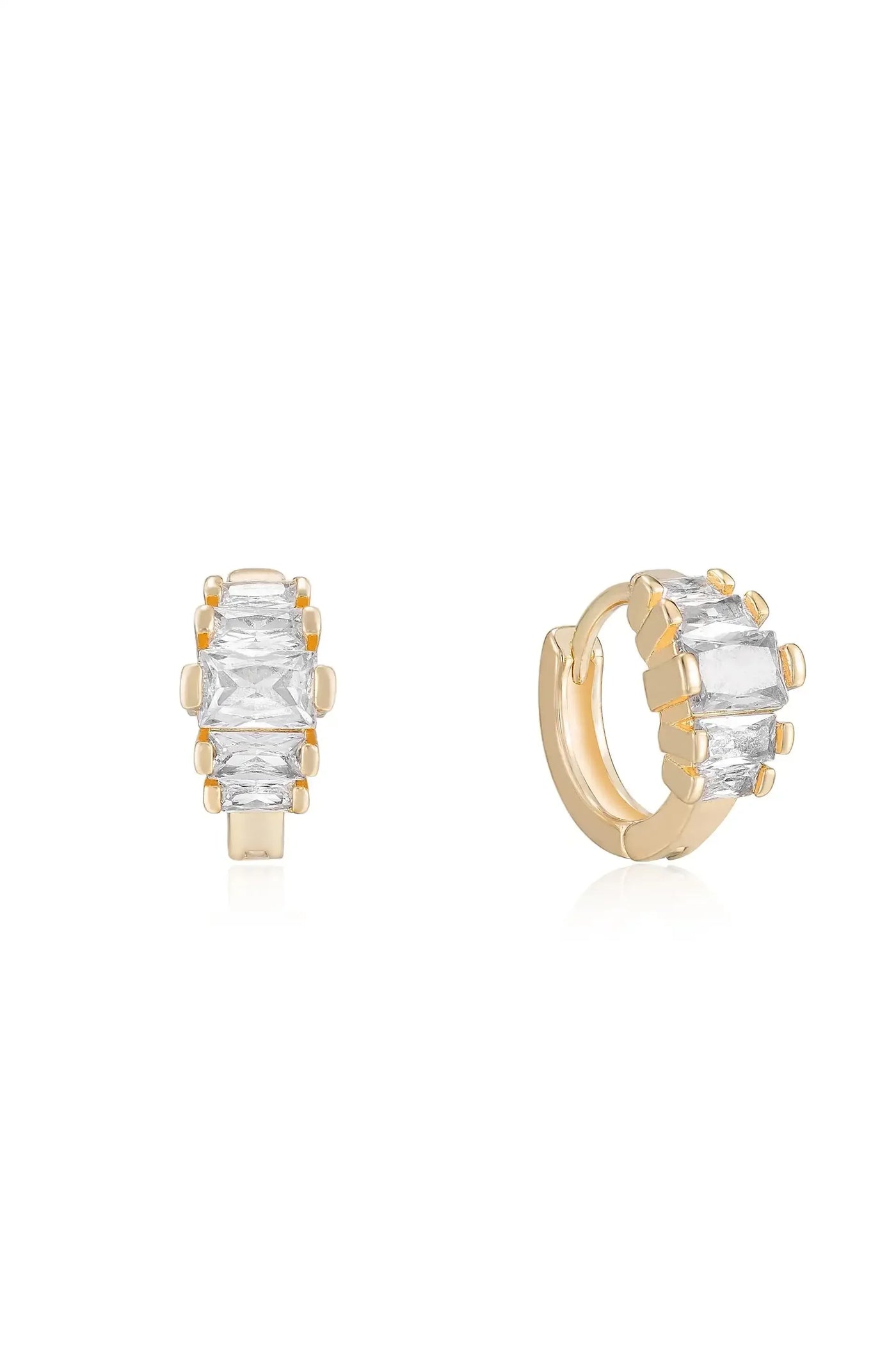 Two gold-tone earrings, one a hoop and the other a stud, each set with rectangular clear stones, rest on a reflective white surface, showcasing their elegant design.