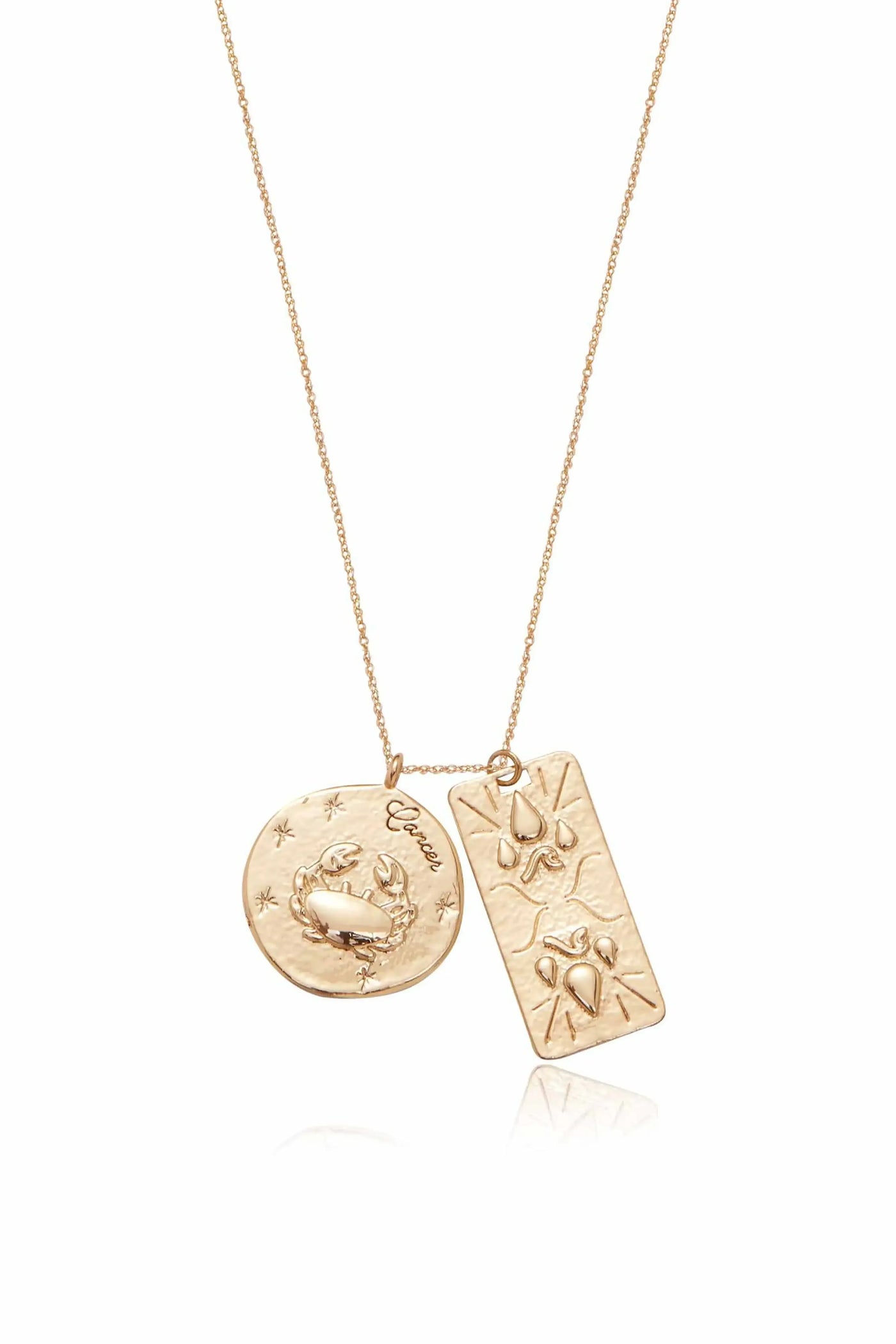 A gold necklace features two pendants: a round one engraved with a crab and the word "Cancer," and a rectangular one with decorative motifs, suspended delicately from a fine chain.