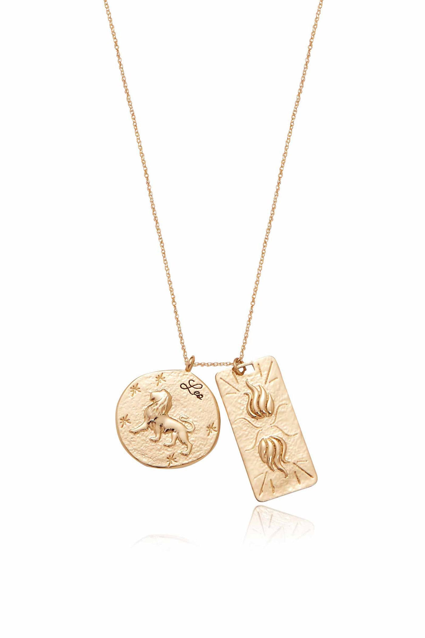 A gold necklace features two pendants: a round charm depicting a lion with “Leo†inscribed, and a rectangular charm with flame-like designs. The background is plain white, emphasizing the jewelry.