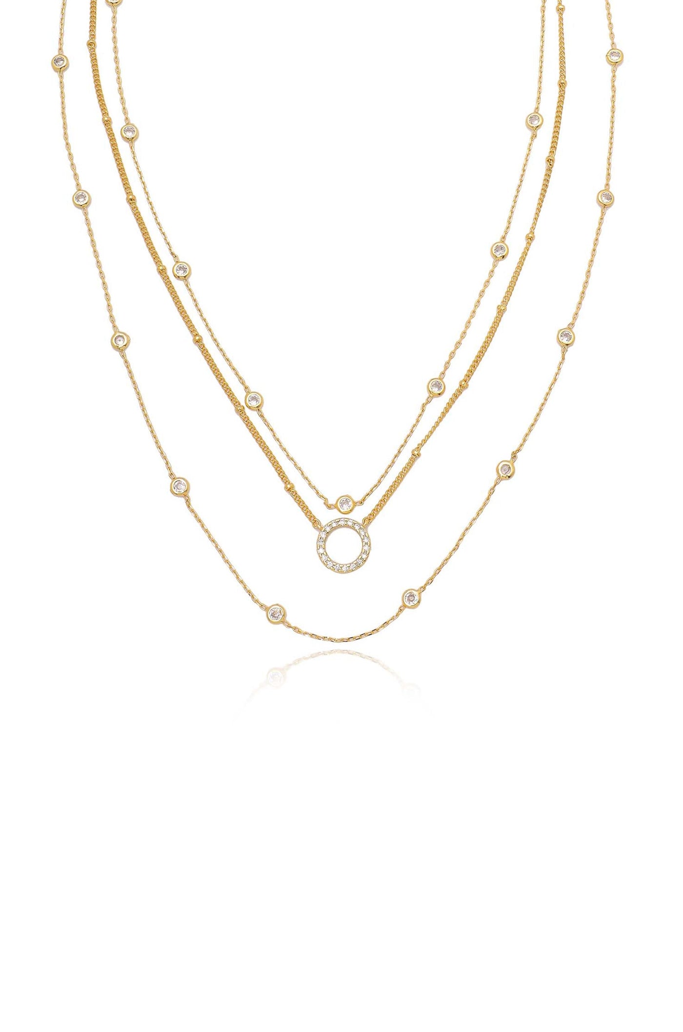 Three delicate gold chains are layered together, featuring round, embellished links and a central circular pendant adorned with stones, set against a plain white background.