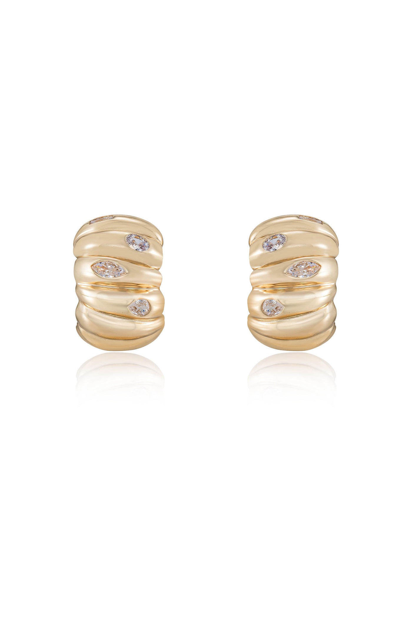 Two gold earrings, featuring a wavy design with scattered, sparkling gemstones. They rest on a reflective surface, enhancing their elegant appearance.