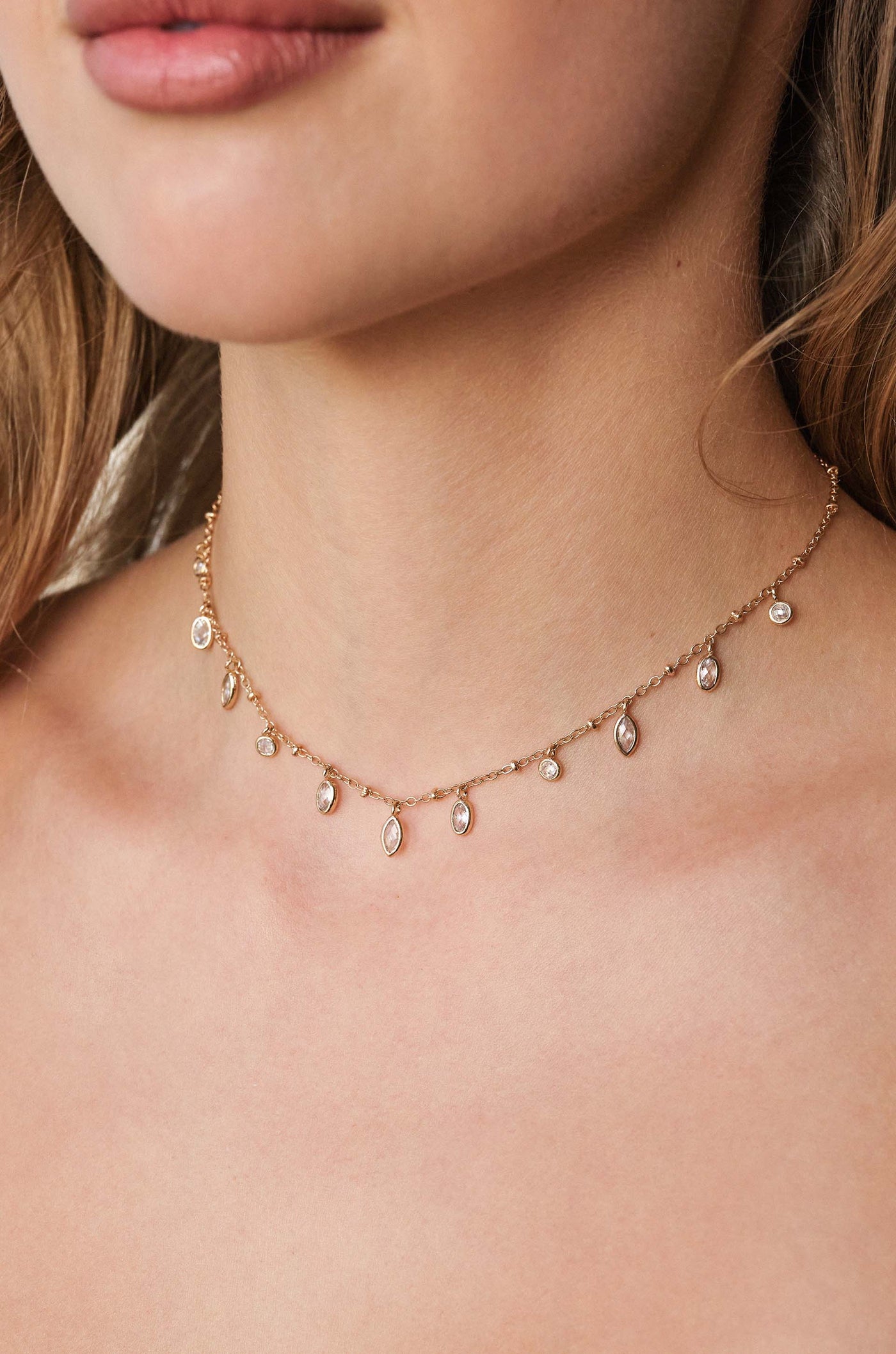 A delicate gold necklace adorned with small, sparkling gems rests on a woman's neck, accentuating her skin. The design features a series of dangling charms that catch the light.