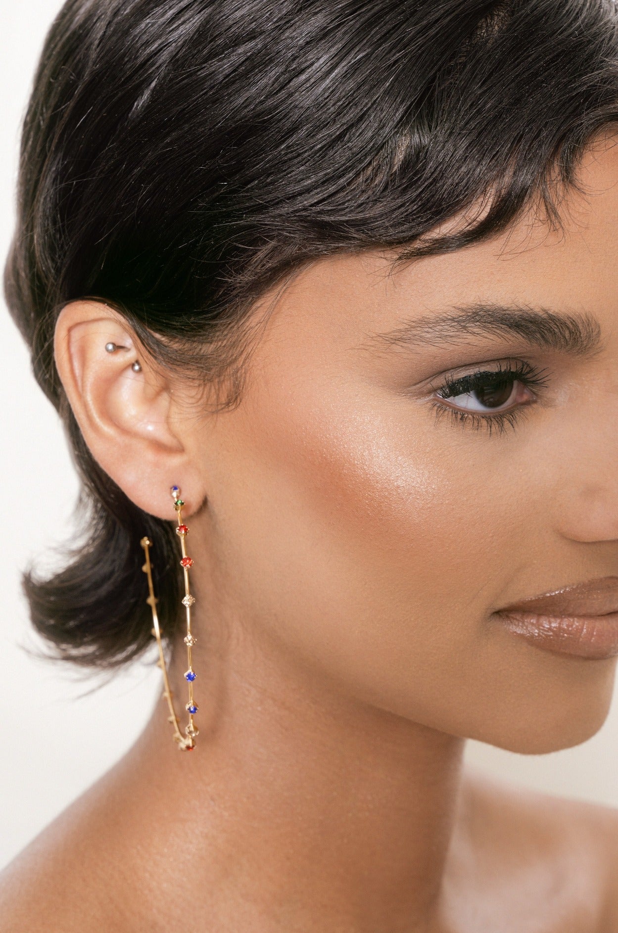 A close-up of a person’s face showcases a sleek bob hairstyle. A long, decorative earring with colorful beads hangs from their ear, set against a neutral background.