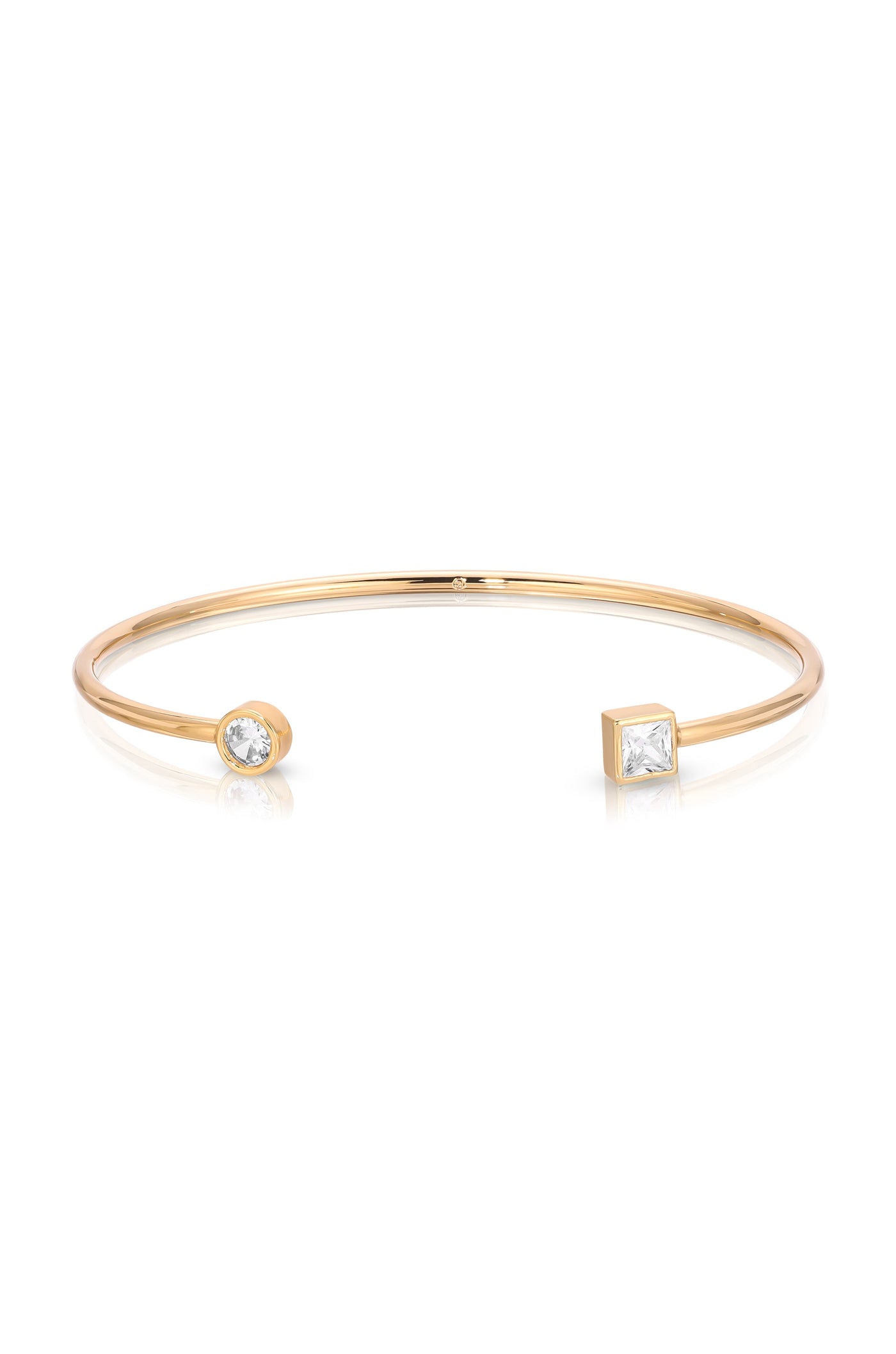 A gold cuff bracelet features two decorative ends, one round and one square, each set with a gemstone. The bracelet has a sleek, minimalist design, shining against a white background.