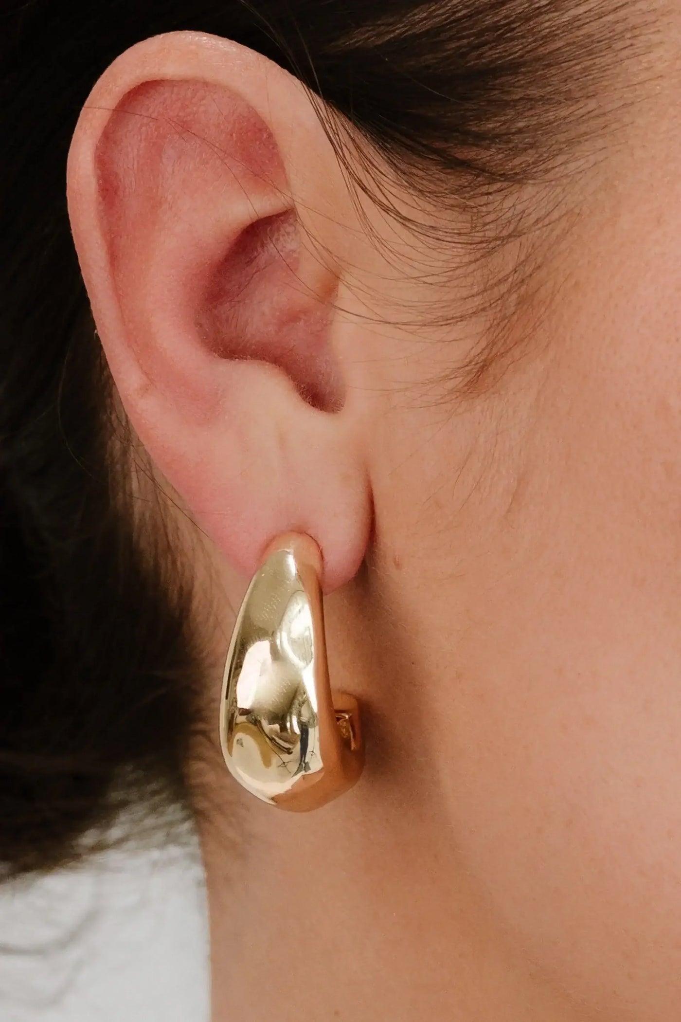 A large, shiny gold earring is prominently displayed on the earlobe, creating a bold accessory contrast against the skin. The background is softly blurred.