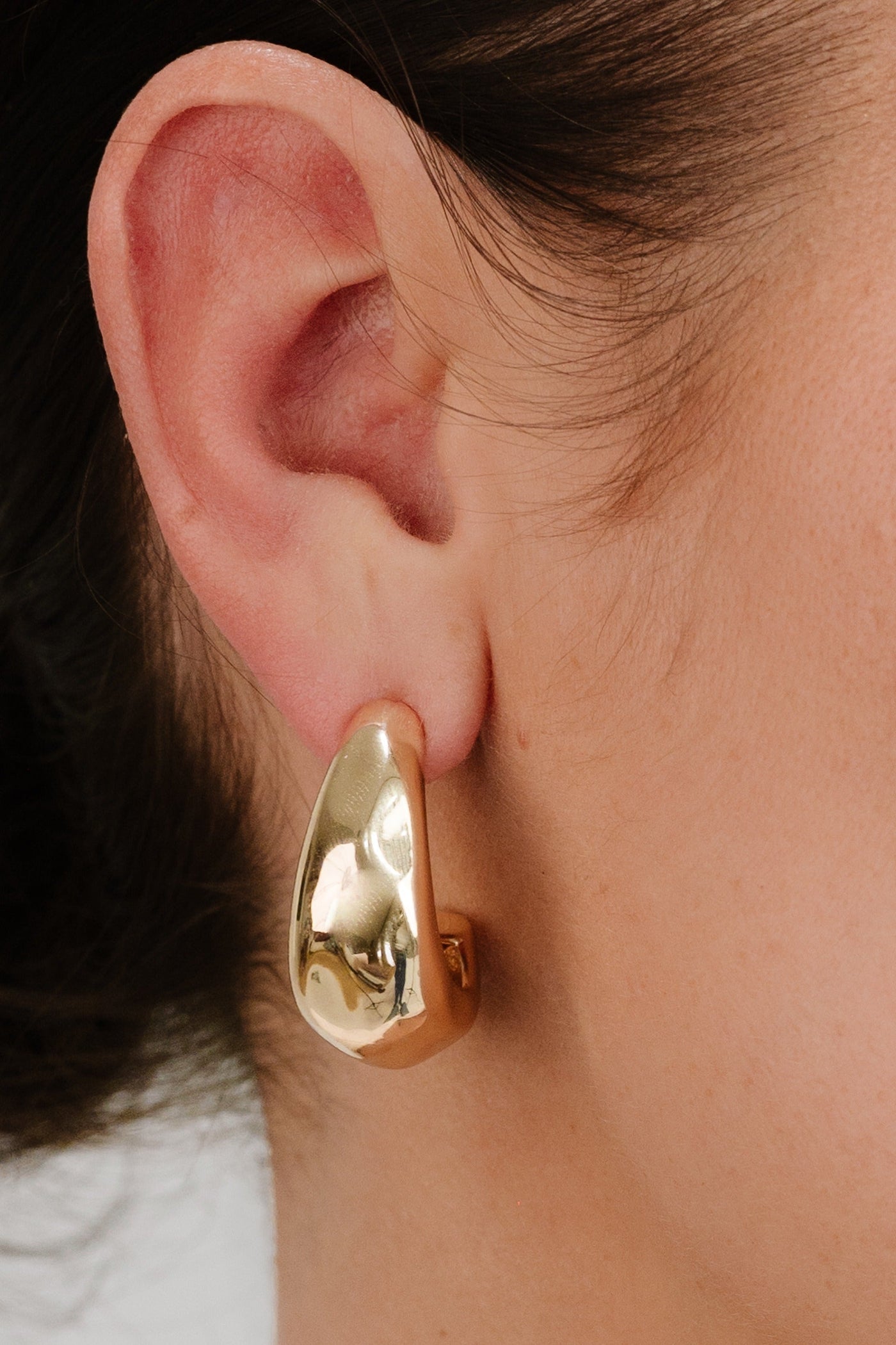 A large, shiny gold earring is prominently displayed on the earlobe, creating a bold accessory contrast against the skin. The background is softly blurred.