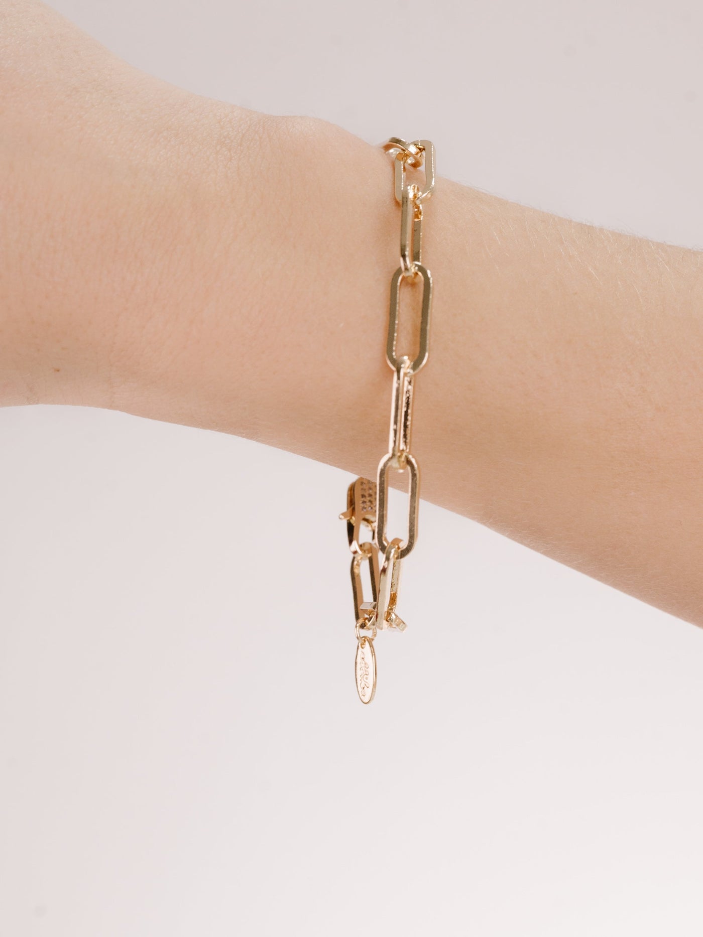 A gold chain bracelet is displayed on a wrist, showcasing its elongated links. The background is light and minimal, emphasizing the bracelet's design and shine.