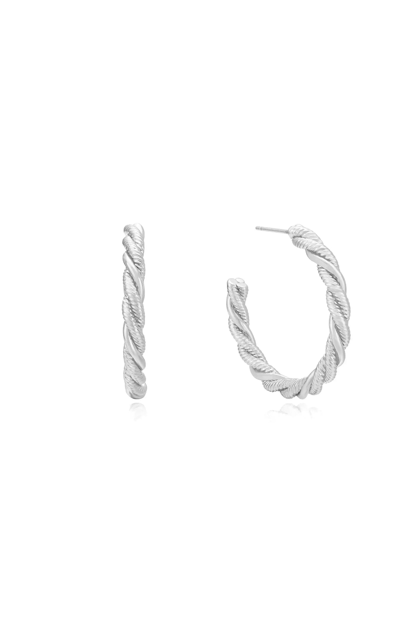Two silver hoop earrings are displayed, one upright and one angled, showcasing a twisted design. They rest on a reflective surface against a plain white background.
