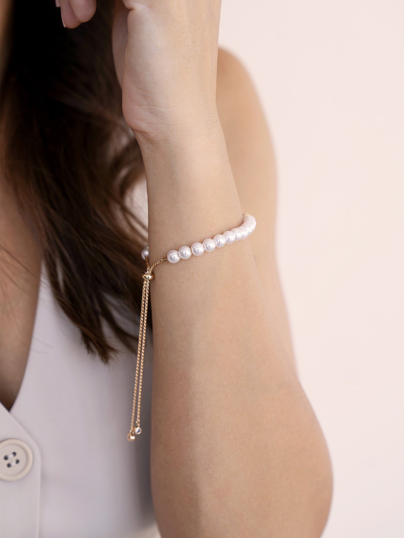 A hand with a bracelet made of pearls rests against a face. The setting features soft, neutral tones that create a gentle and elegant atmosphere.