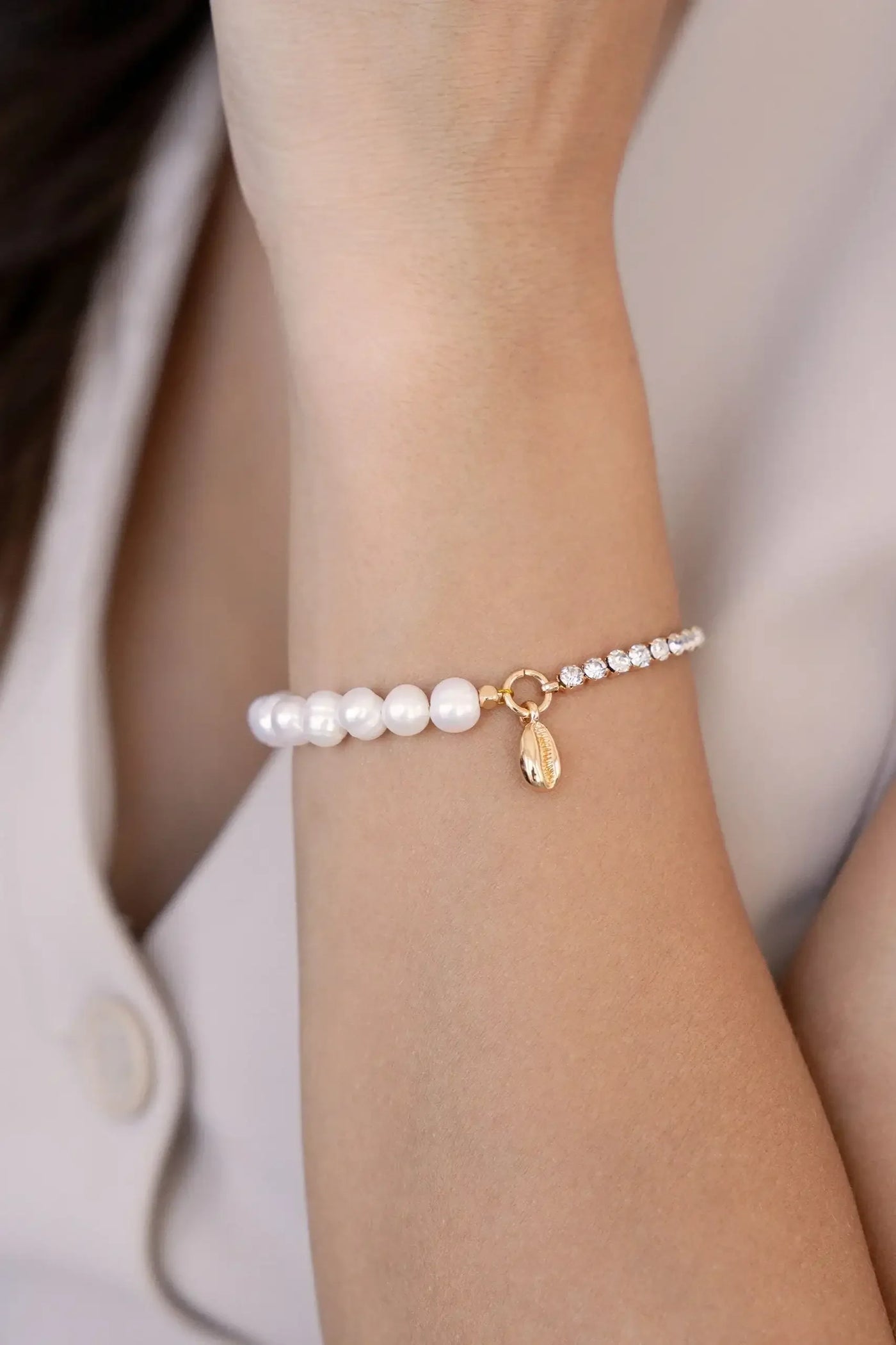 A bracelet made of alternating pearls and sparkling gems adorns a person's wrist. The wrist is exposed, with a blurred background of light fabric and skin, suggesting a casual setting.