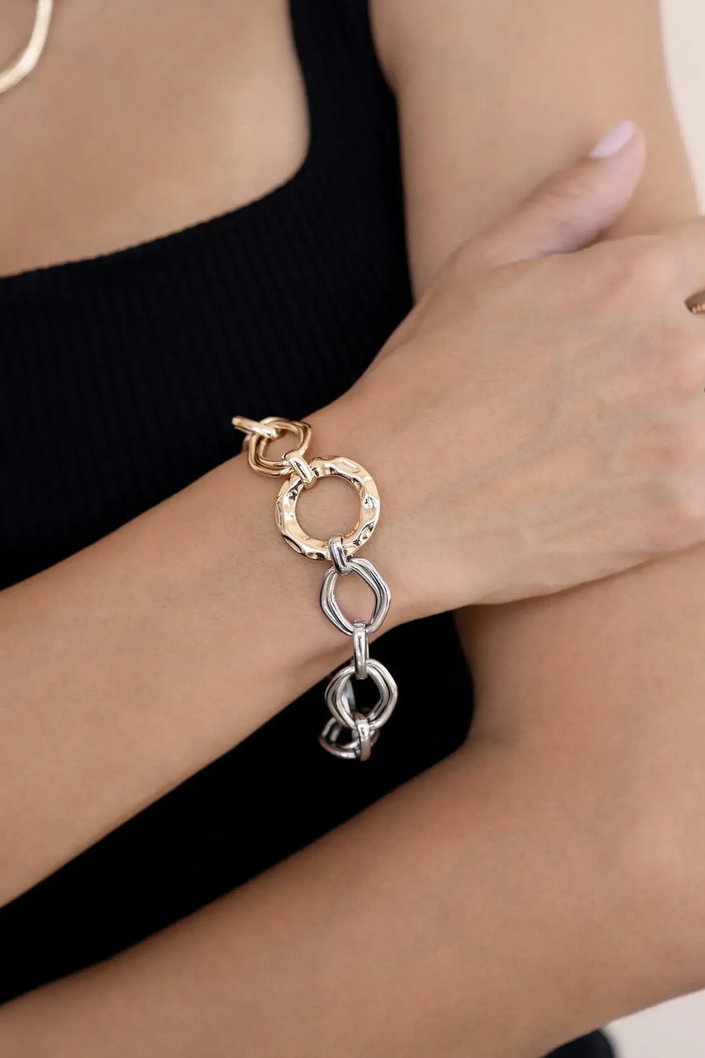 A hand wearing a stylish metal bracelet is shown. The bracelet features interconnected gold and silver links. The background is neutral, enhancing the focus on the accessory.
