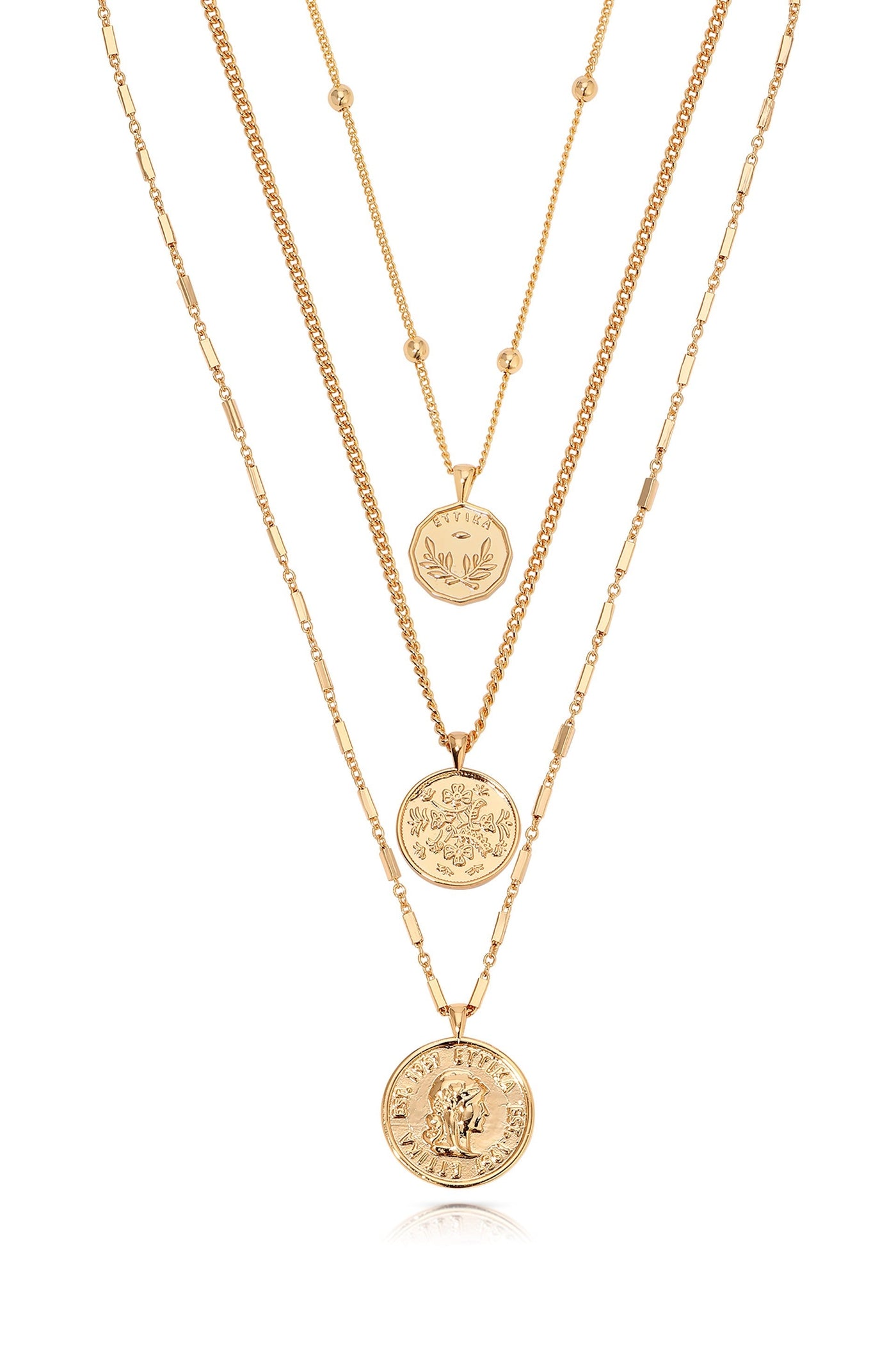 Three layered gold necklaces are displayed. Each necklace features circular pendants with intricate designs, hanging gracefully against a neutral background, showcasing their elegance and shine.