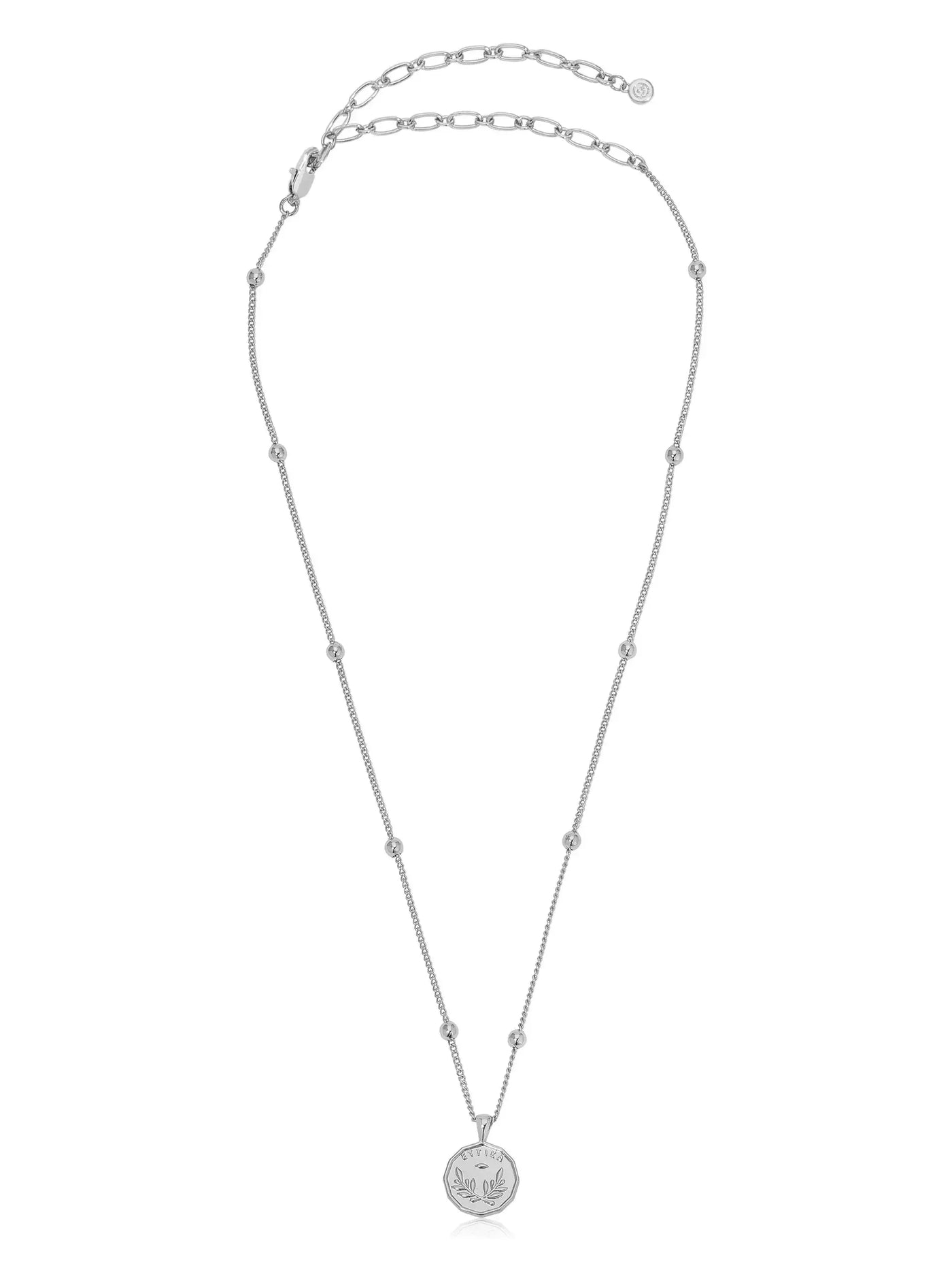 A silver necklace features a delicate chain with small round beads and a circular pendant adorned with a leaf design, suspended in a neutral, soft-lit background.