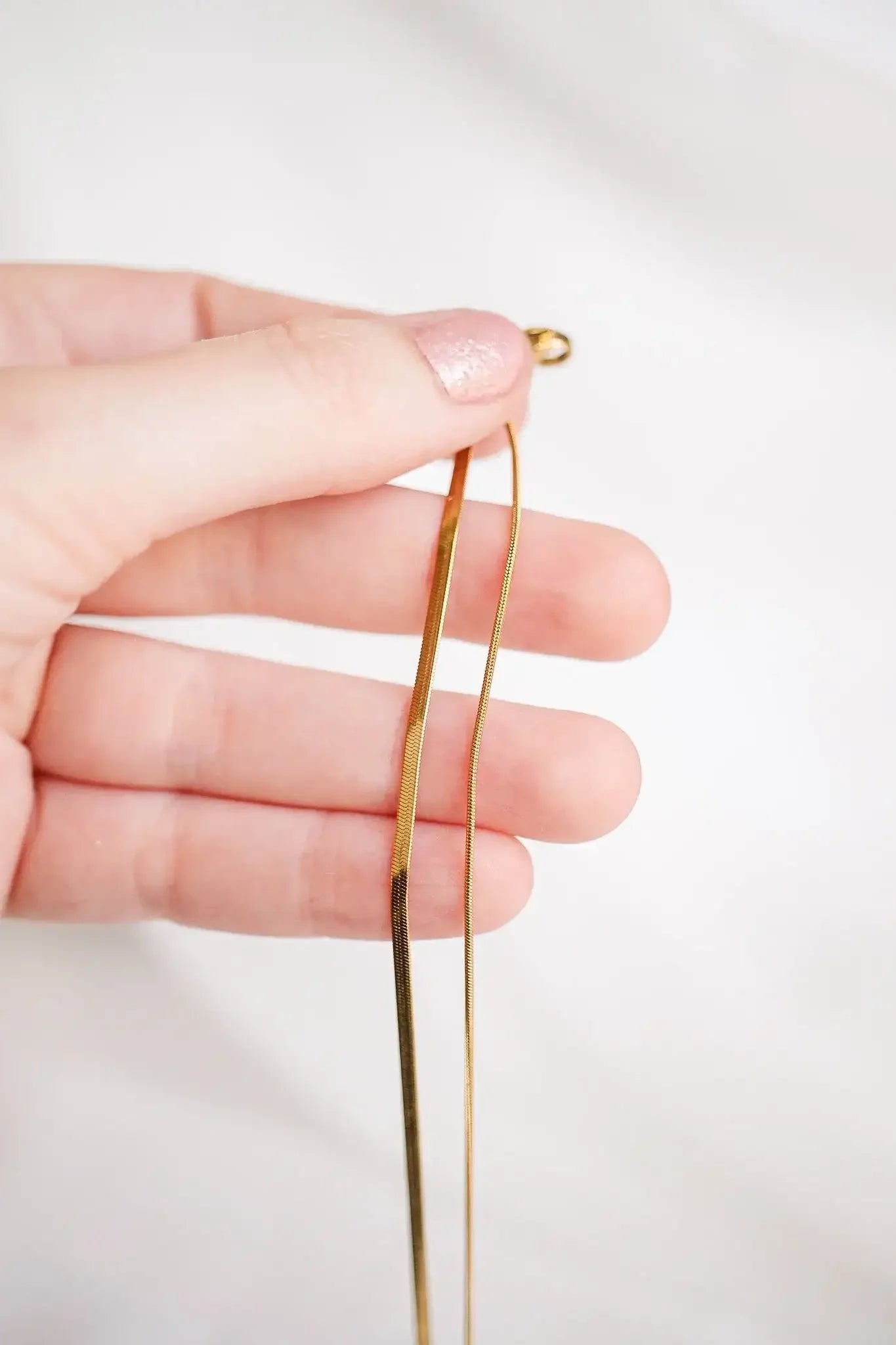 A hand holds a pair of gold-colored hairpins. The pins are straight, one slightly longer than the other, against a light, neutral background.