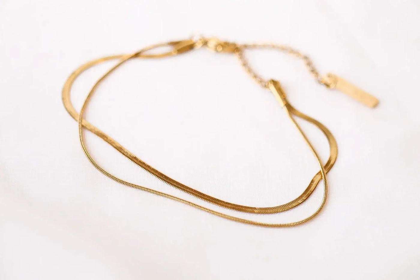 A delicate gold bracelet lies on a soft, light-textured surface. The bracelet features multiple slender loops intertwined, showcasing a simple yet elegant design.
