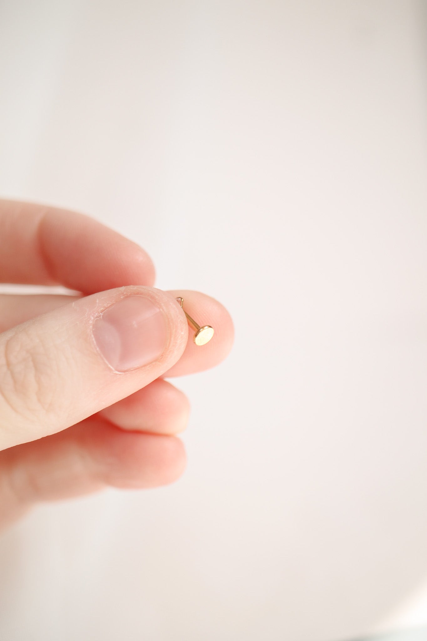 A hand holds a small gold earring. The action involves the person possibly examining or showcasing the earring. The background is softly blurred, enhancing the focus on the object.