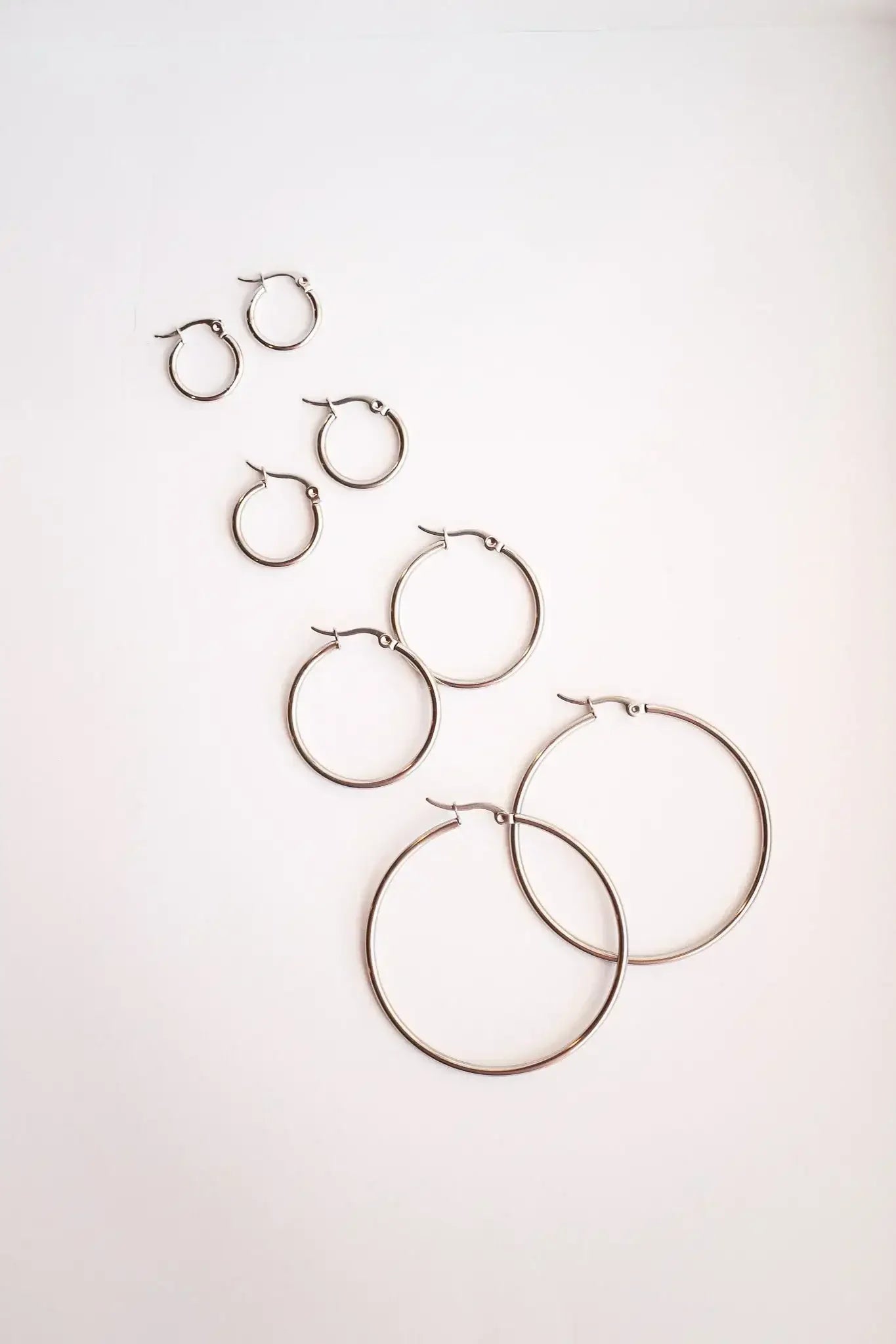 Several pairs of metallic hoop earrings, varying in size, arranged in a diagonal pattern on a pale background, showcasing their shine and design.