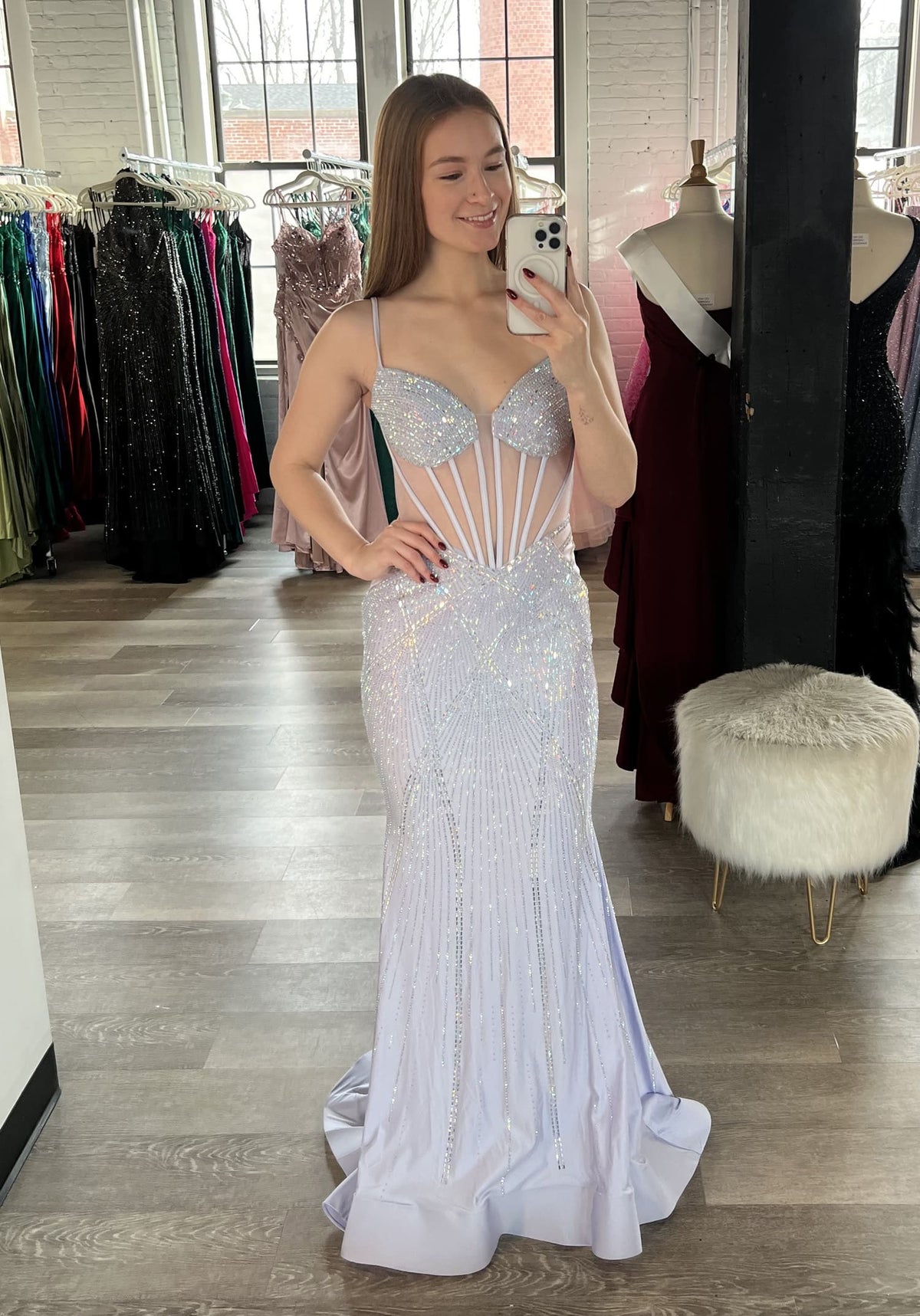 A woman takes a mirror selfie in a bridal salon wearing a sparkling white mermaid gown with a sheer corset-style bodice and beaded details.