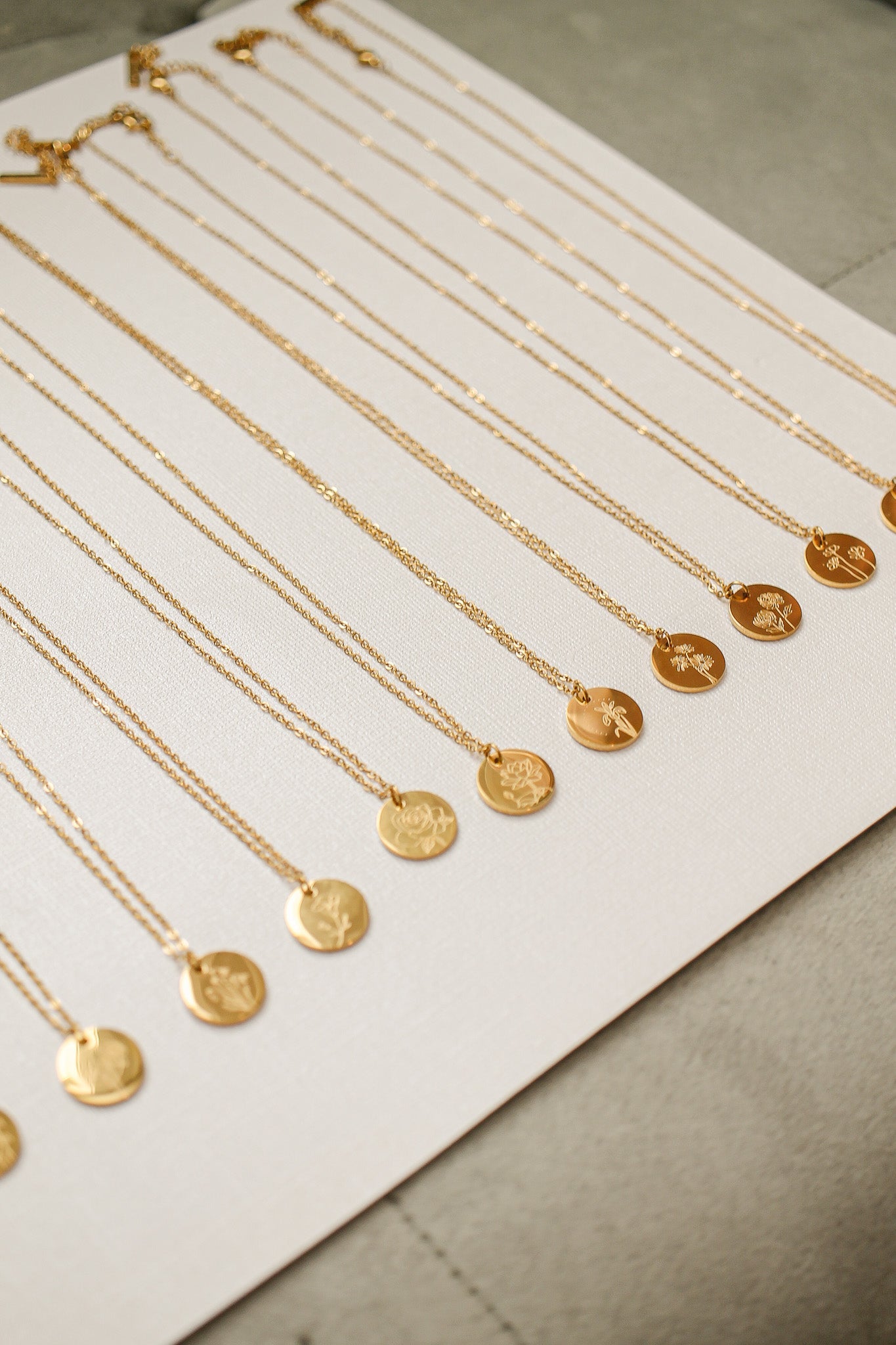 Gold necklaces with circular pendants, some engraved, are neatly arranged on a light fabric background. The jewelry is presented in a way that highlights their intricate designs and varying lengths.