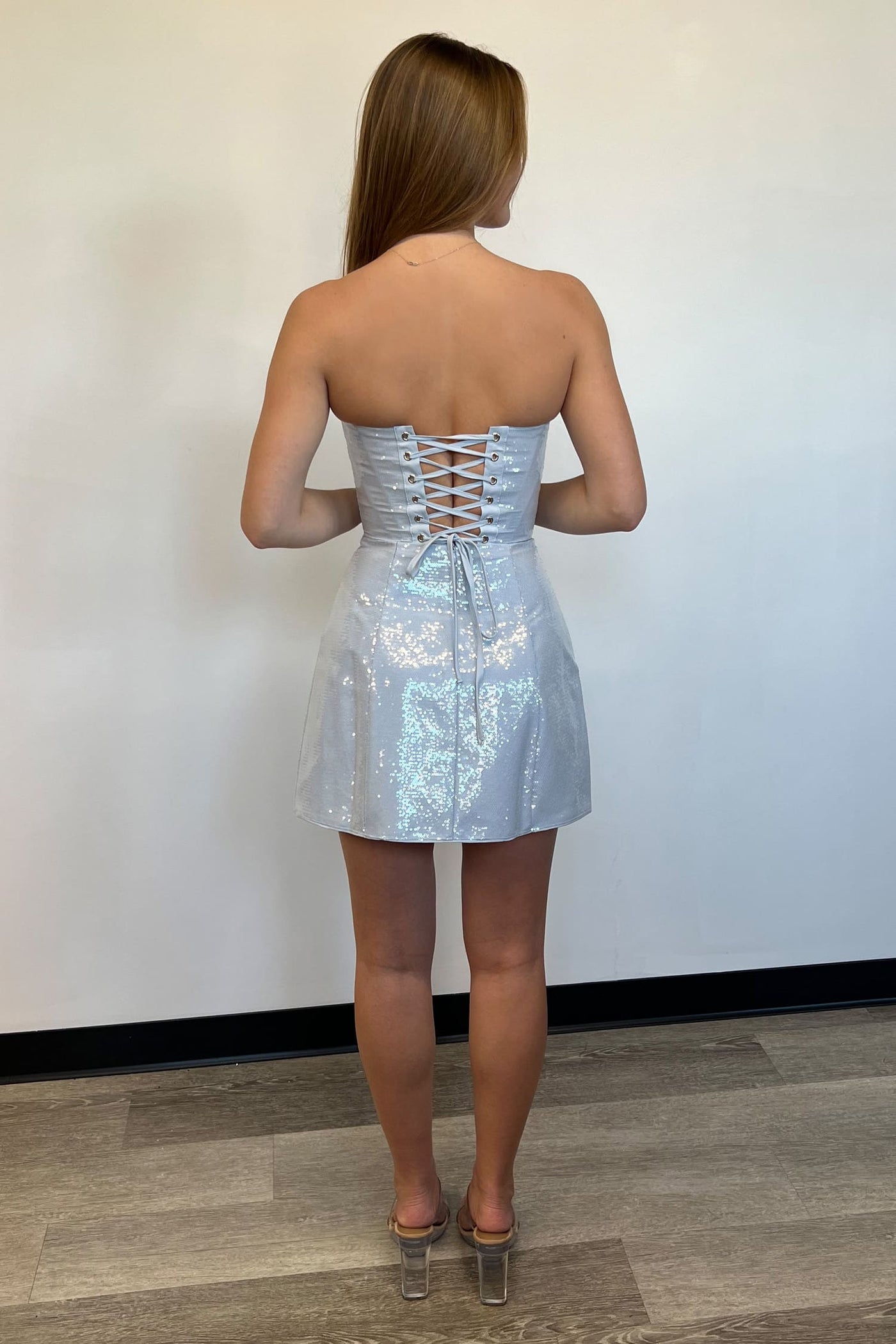 Woman wearing a strapless silver sequin dress against a white wall.